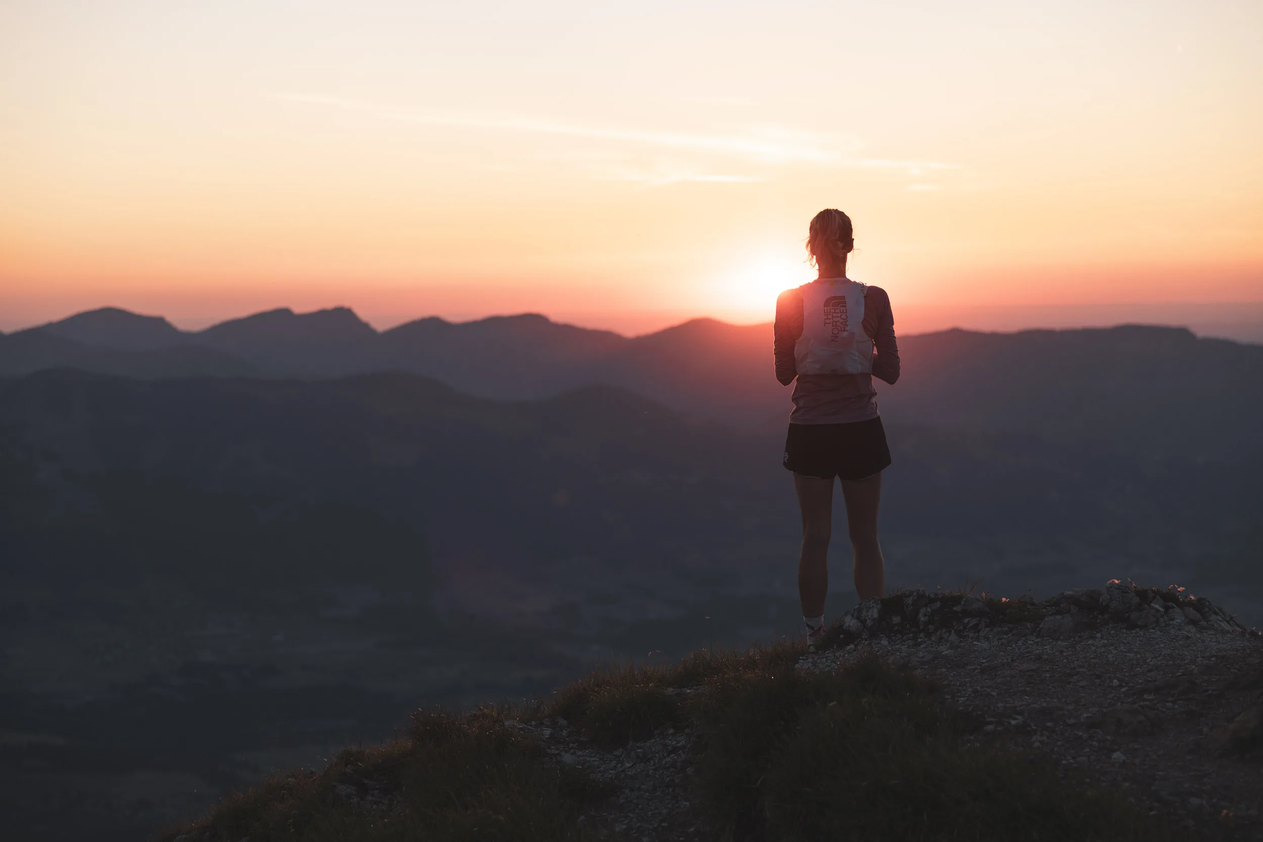 Silhouette einer Trailrunnerin vor der untergehenden Sonne über den Bergen