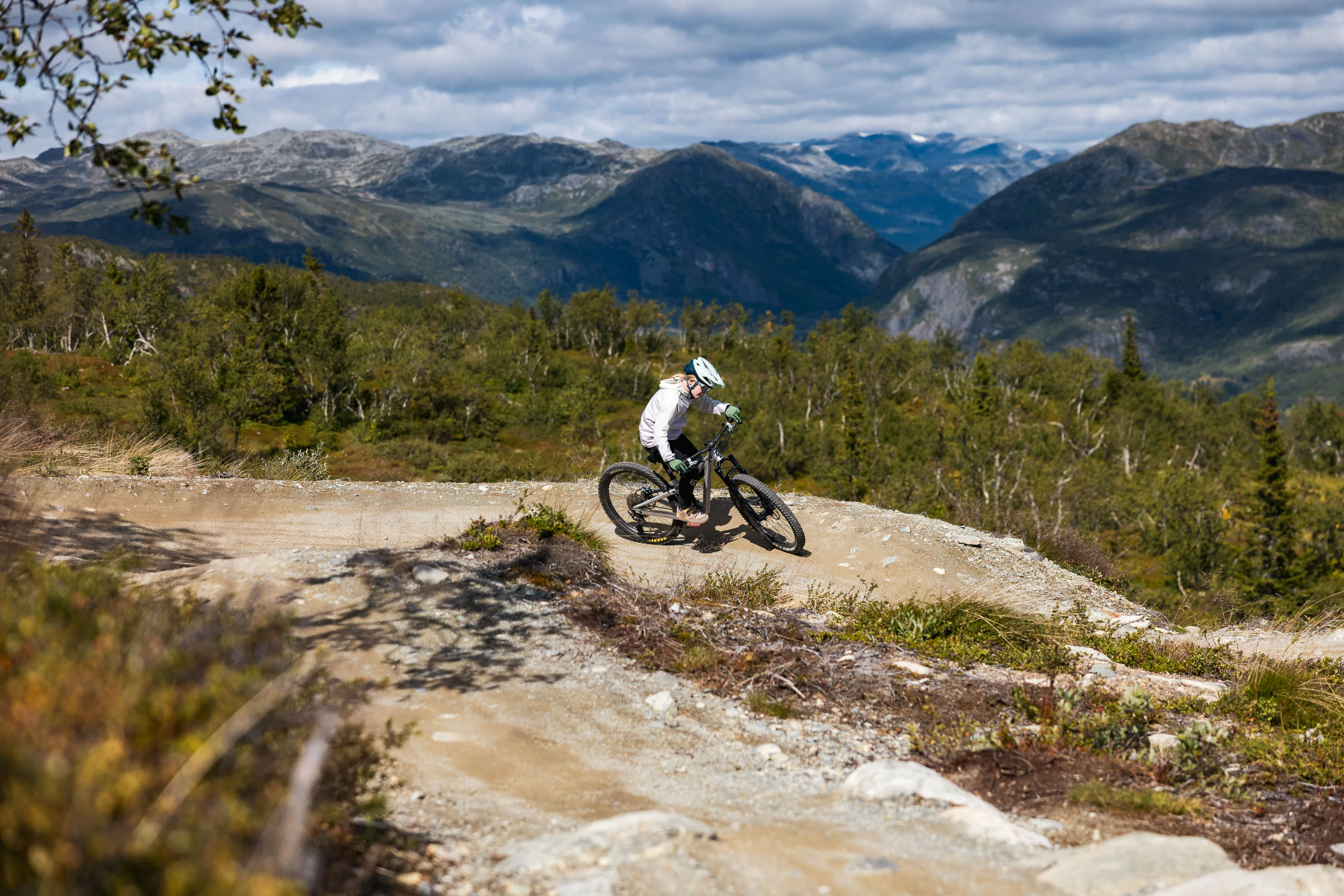 Mountainbiker fährt durch einen staubigen Anlieger mit Bergen im Hintergrund