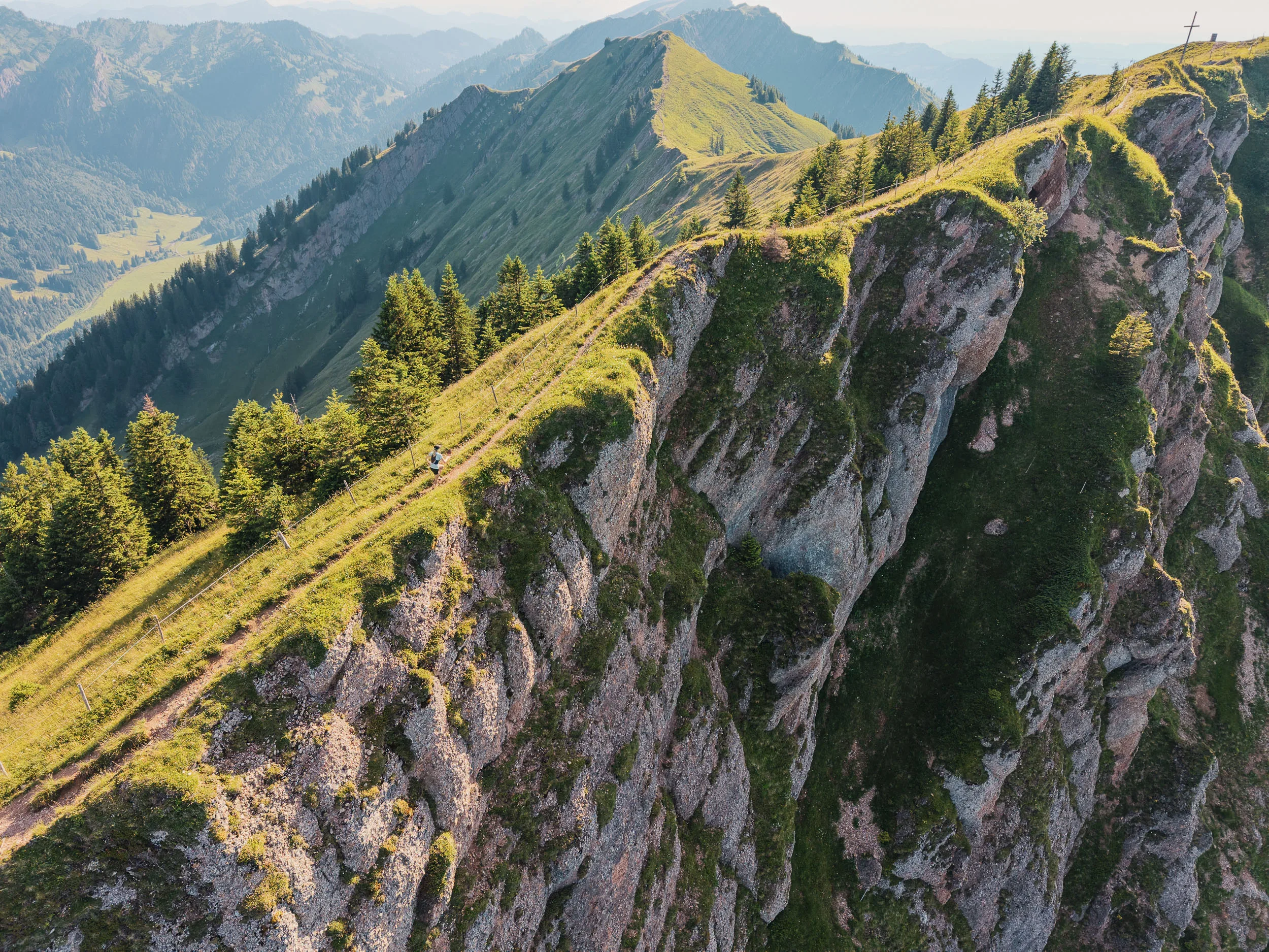 Eine Trailrunnerin läuft auf einem schmalen Grat über steilen Felswänden der Nagelfluhkette.