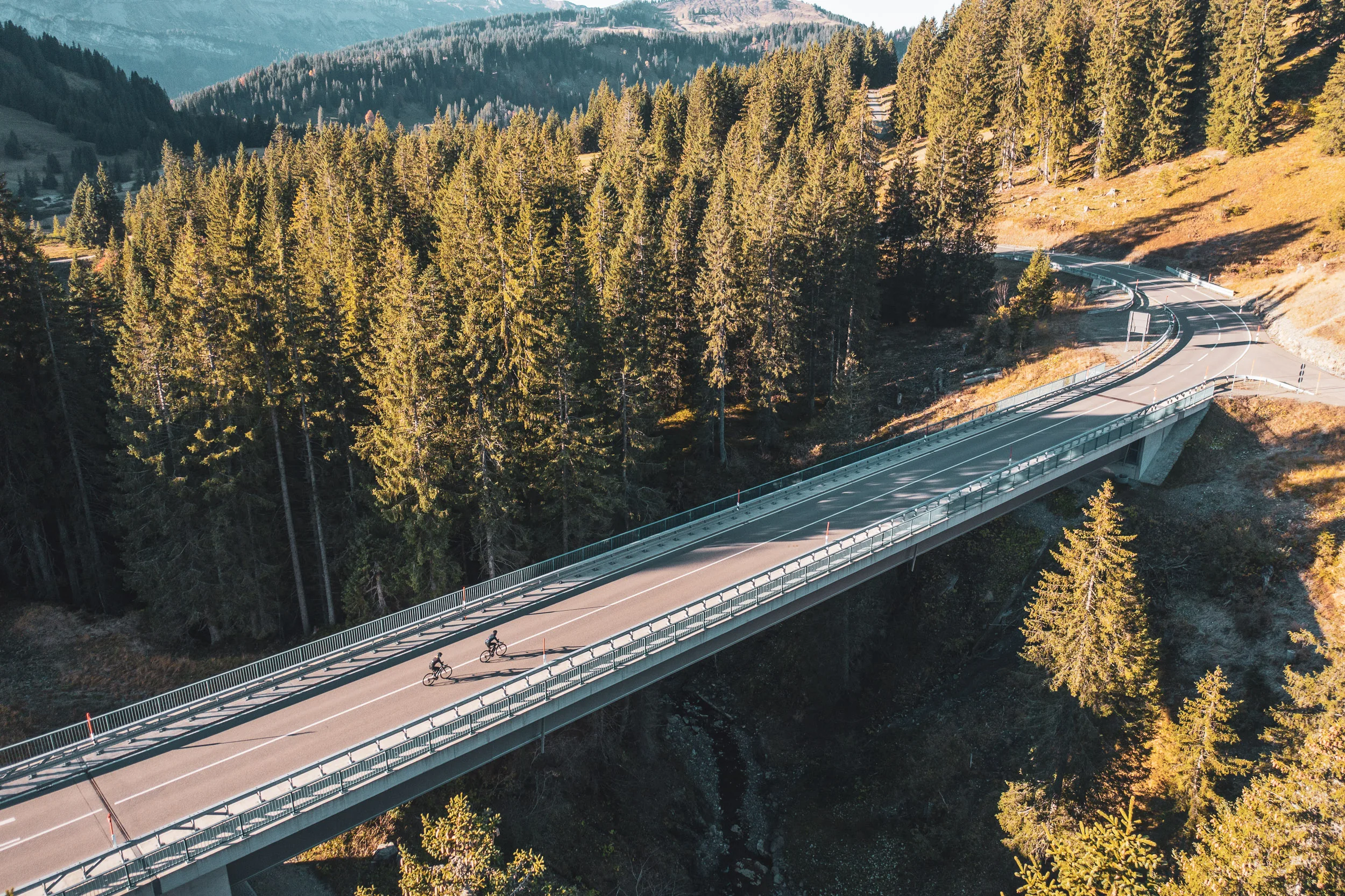 Zwei Rennradfahrerinnen überqueren eine Brücke über einem bewaldeten Bergtal