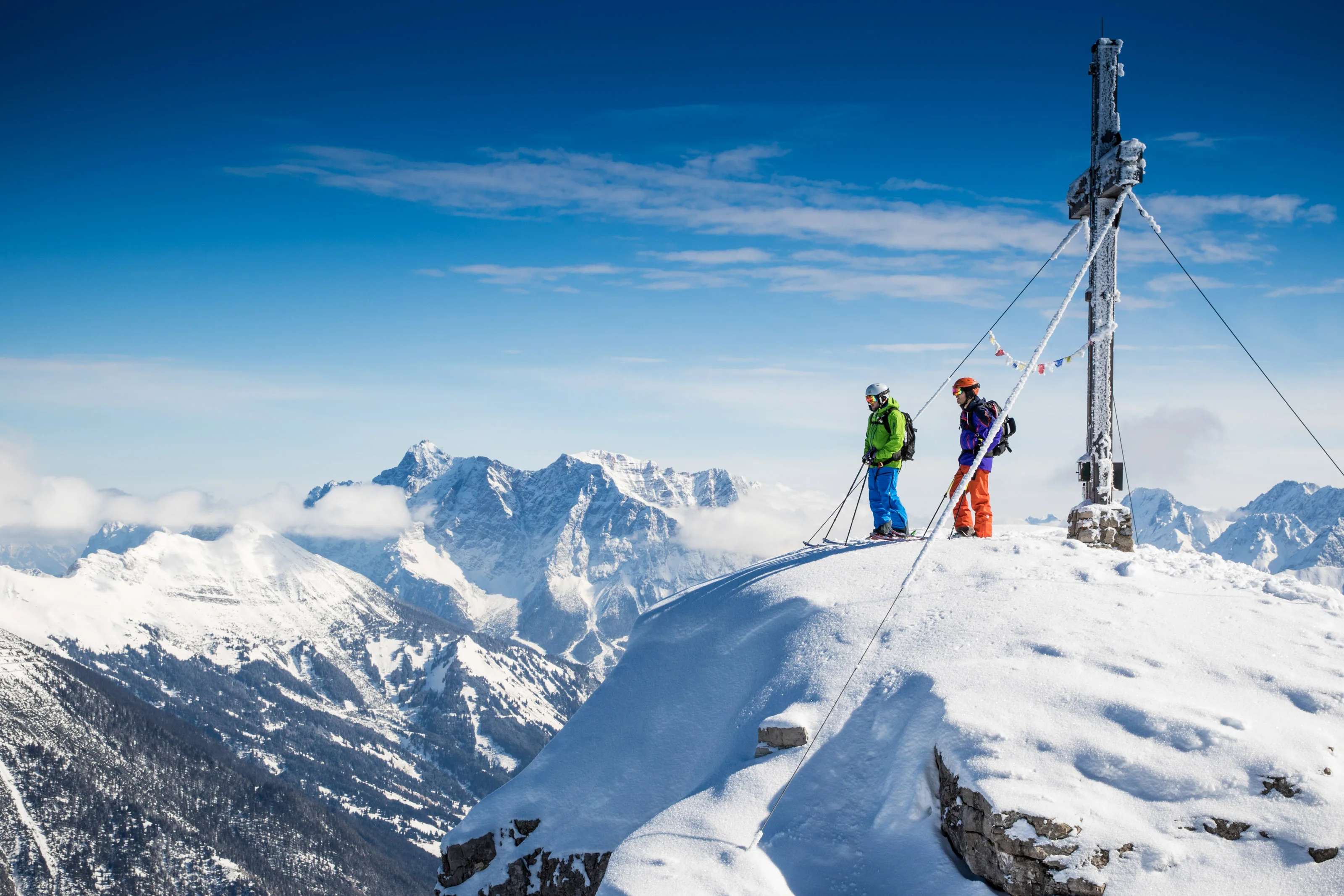 Florian Häusler und Florian Bergmann mit Skiern am Gipfelkreuz des Thaneller.