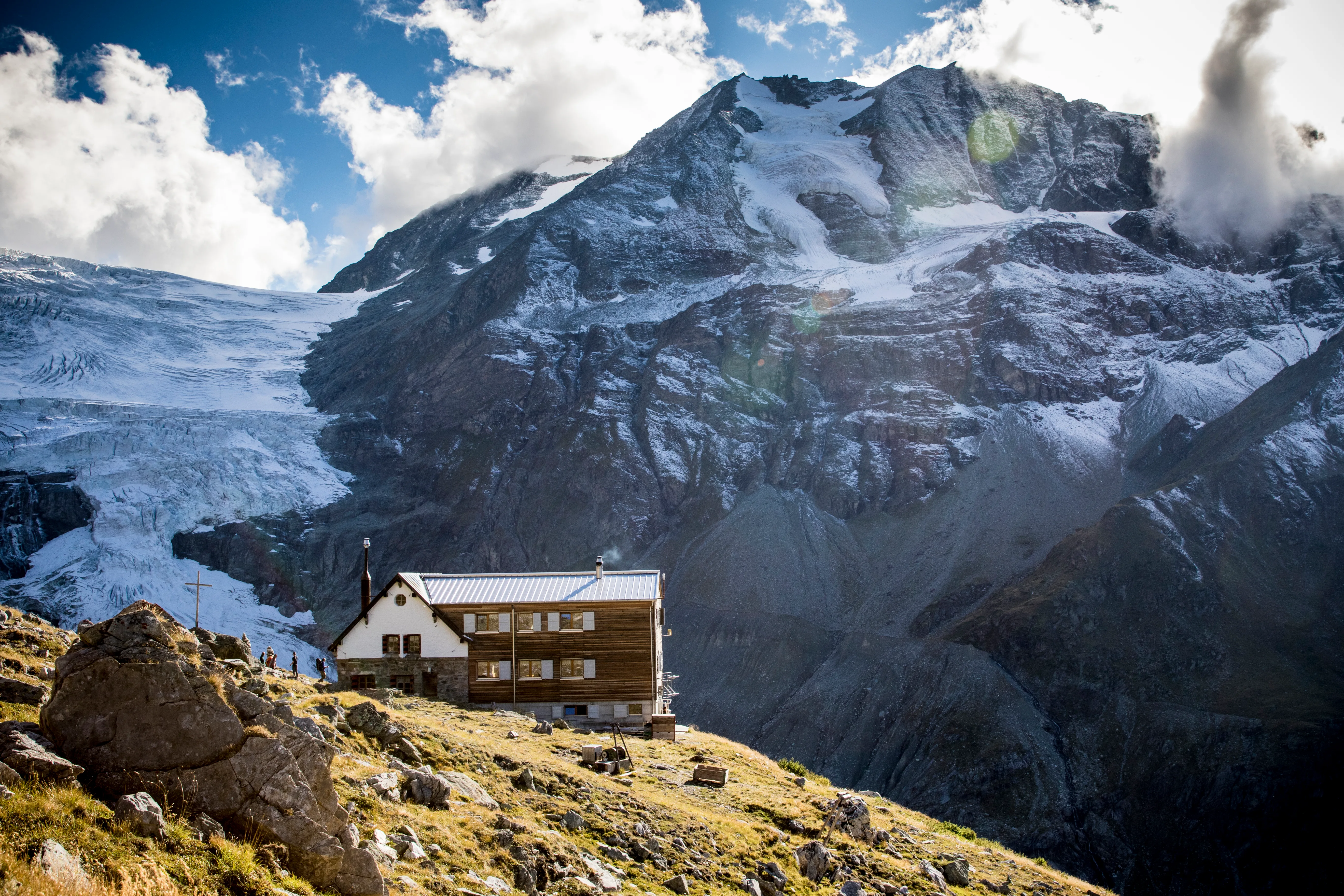 Eine Berghütte steht unter einer schroffen, hochalpinen Gipfelflanke im Wallis.