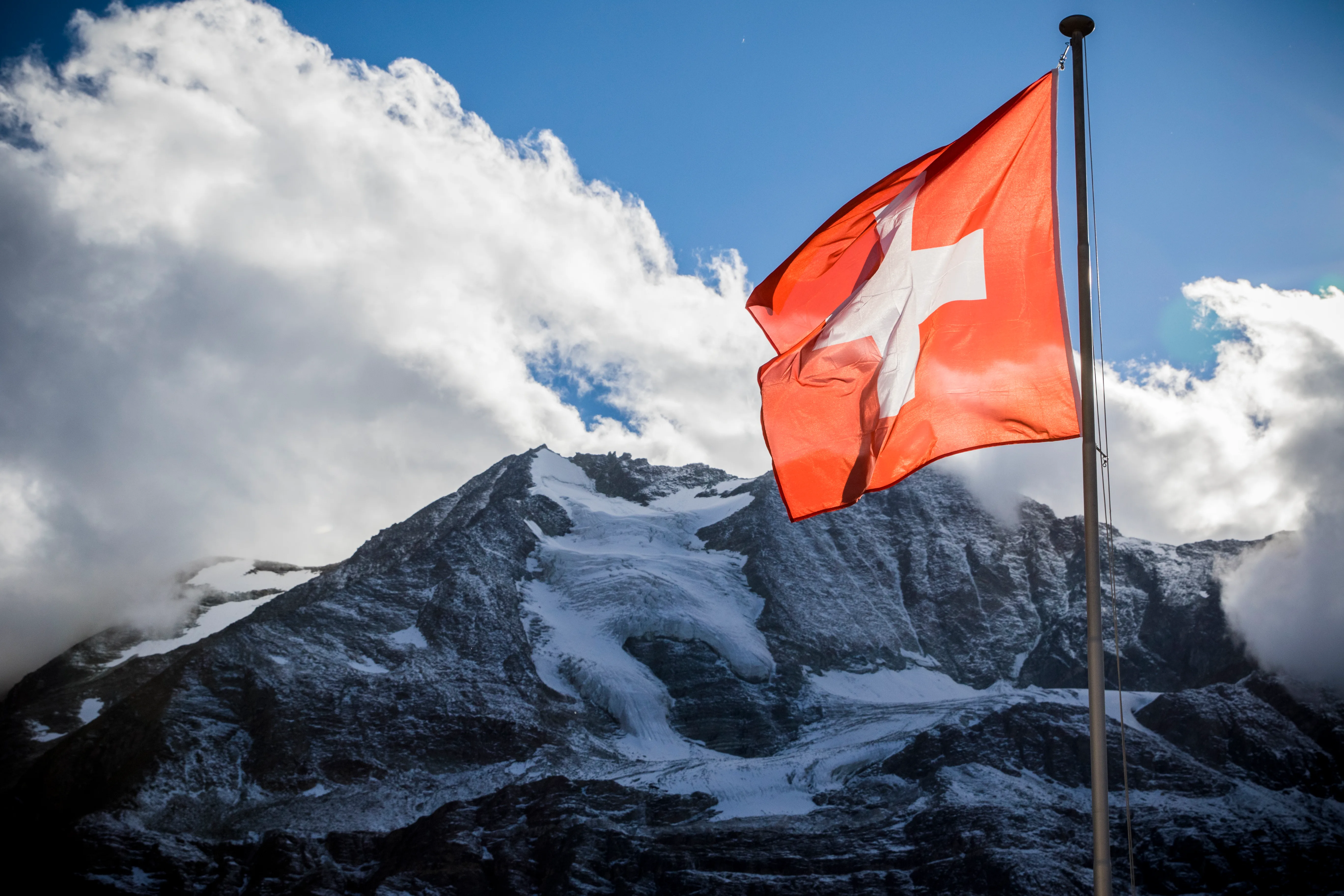 Eine Schweizer Flagge weht vor einem verschneiten Gipfel im hochalpinen Wallis.