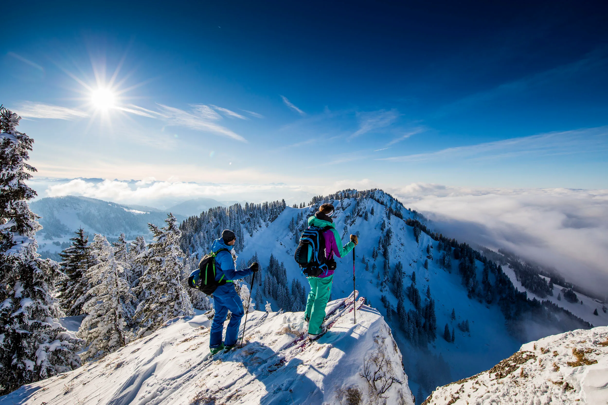 Drei Skitourengeher stehen über einem wolkenverhangenen Wintertal.