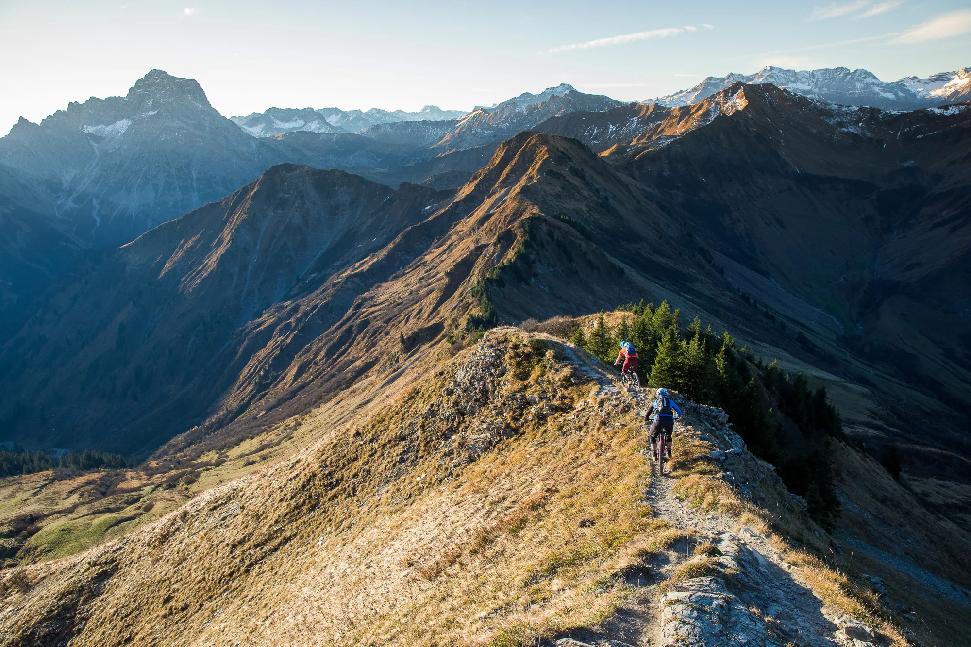 Mountainbiker folgen einem schmalen Weg über einen sonnenbeschienenen Grat vor dunklen Bergen