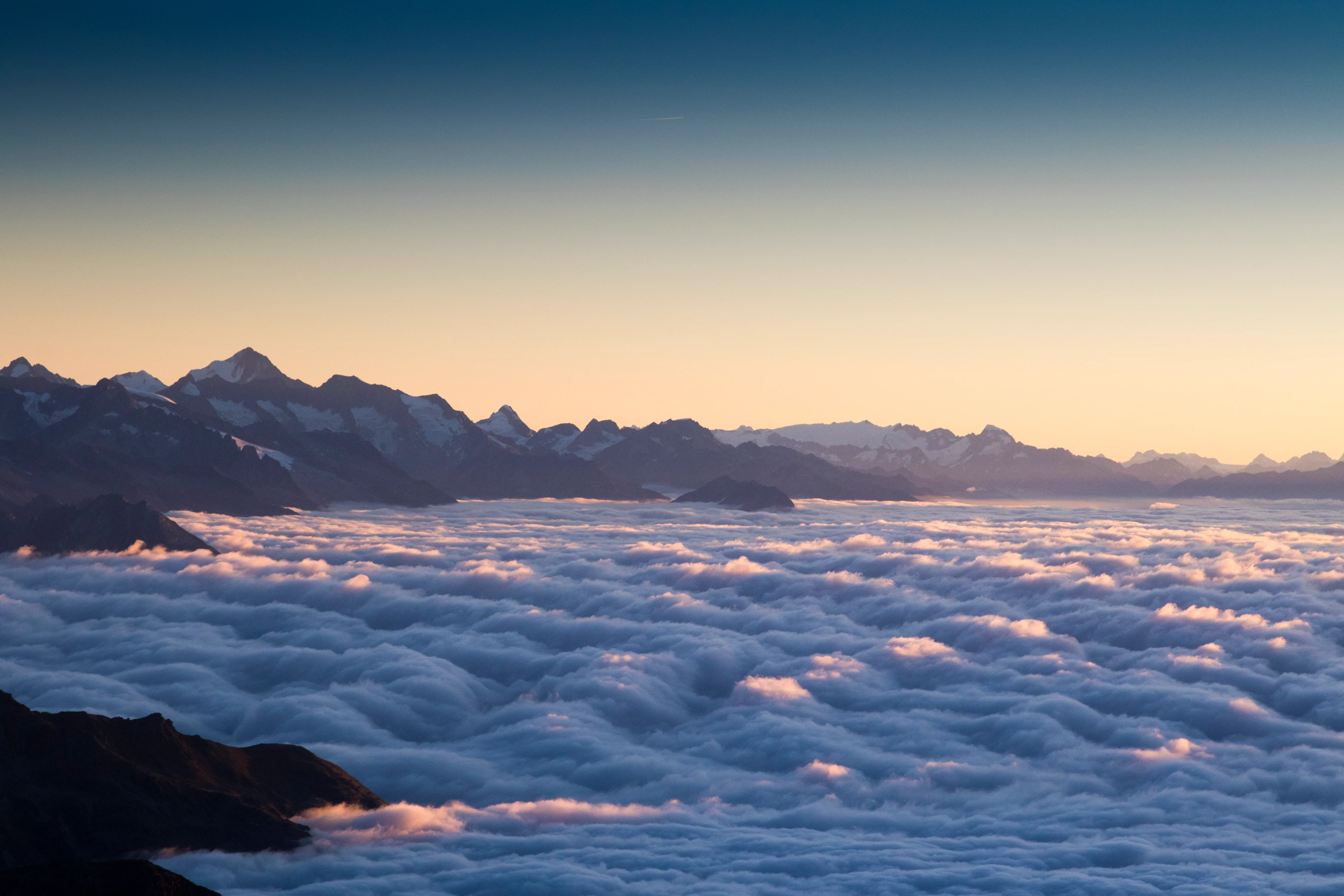 Dunkle Bergsilhouetten stehen über einem weiten Wolkenmeer im Wallis.