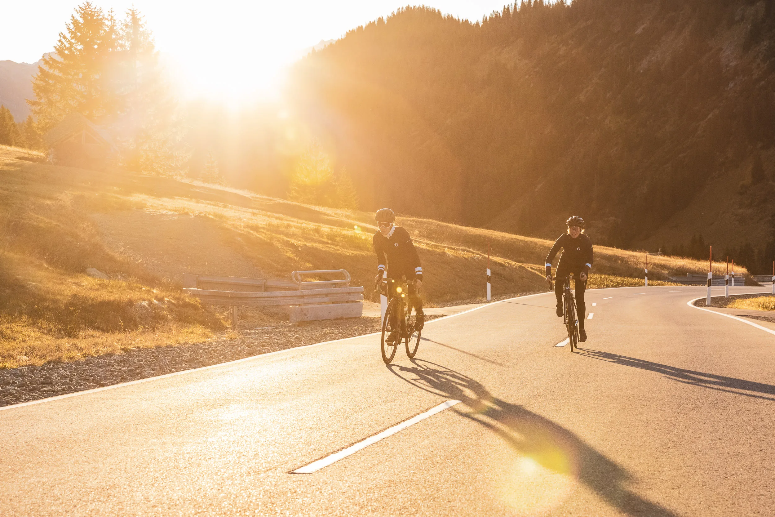 Zwei Rennradfahrerinnen fahren auf einer Kurve im tiefen Sonnenlicht