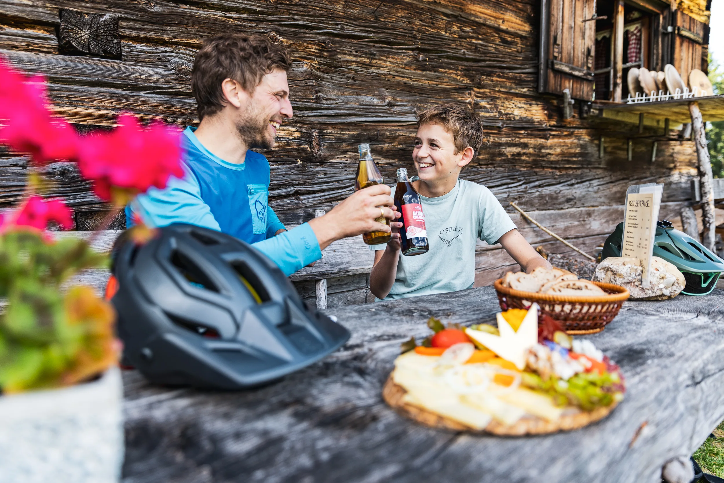 Zwei Mountainbiker stoßen vor der Holzhütte der Alpe Gschwenderberg an