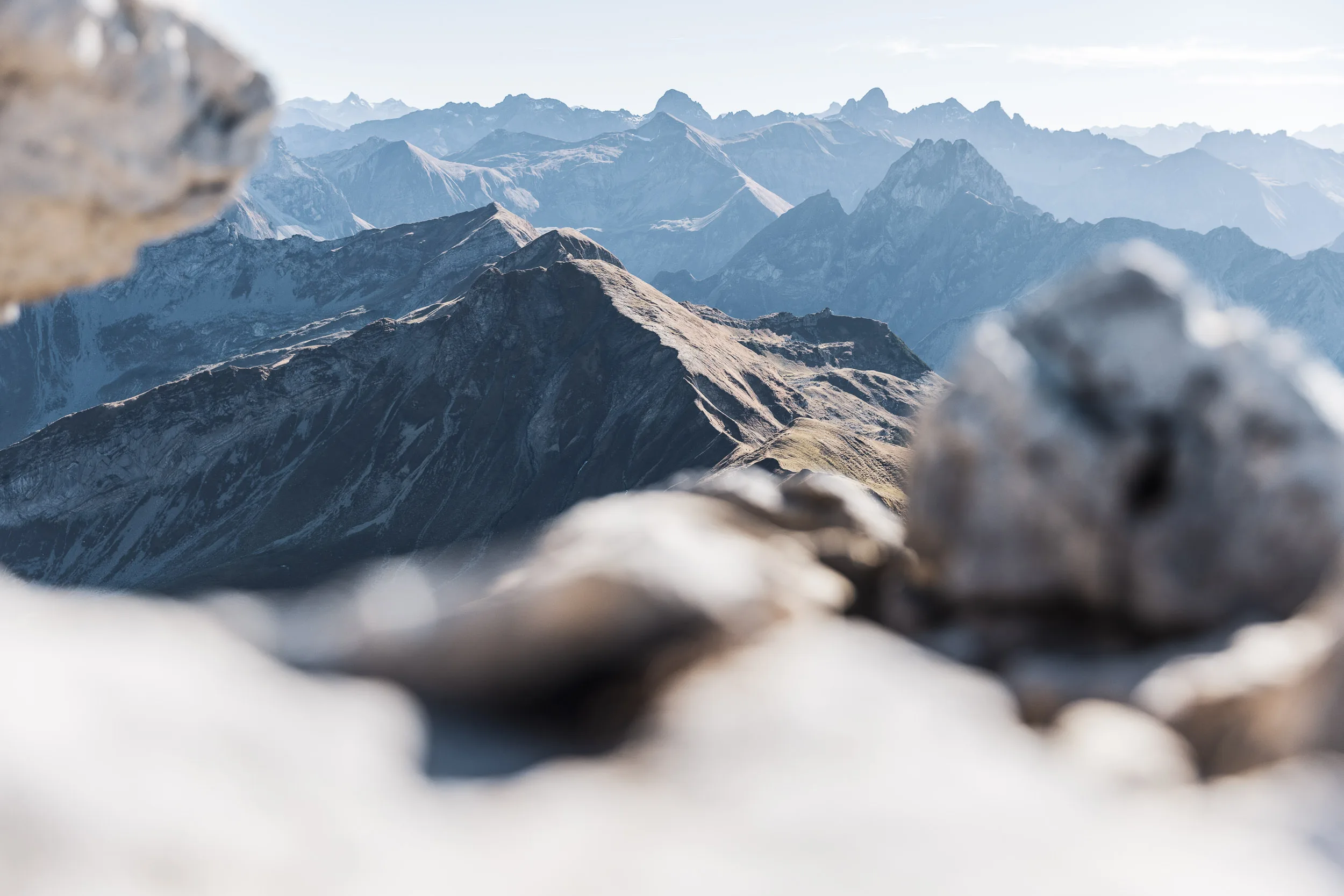 Nahe Kalkfelsen rahmen einen sonnigen Grat und ferne Bergketten im Dunst.