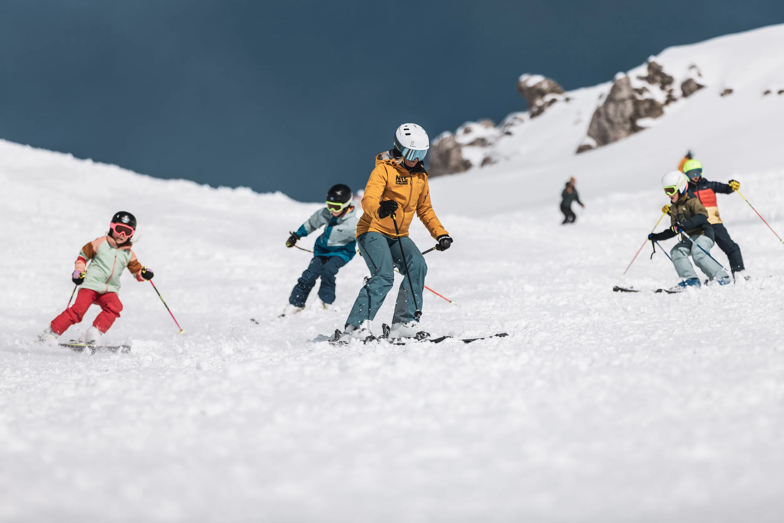 Skilehrer und Kinder fahren gemeinsam über eine verschneite Piste
