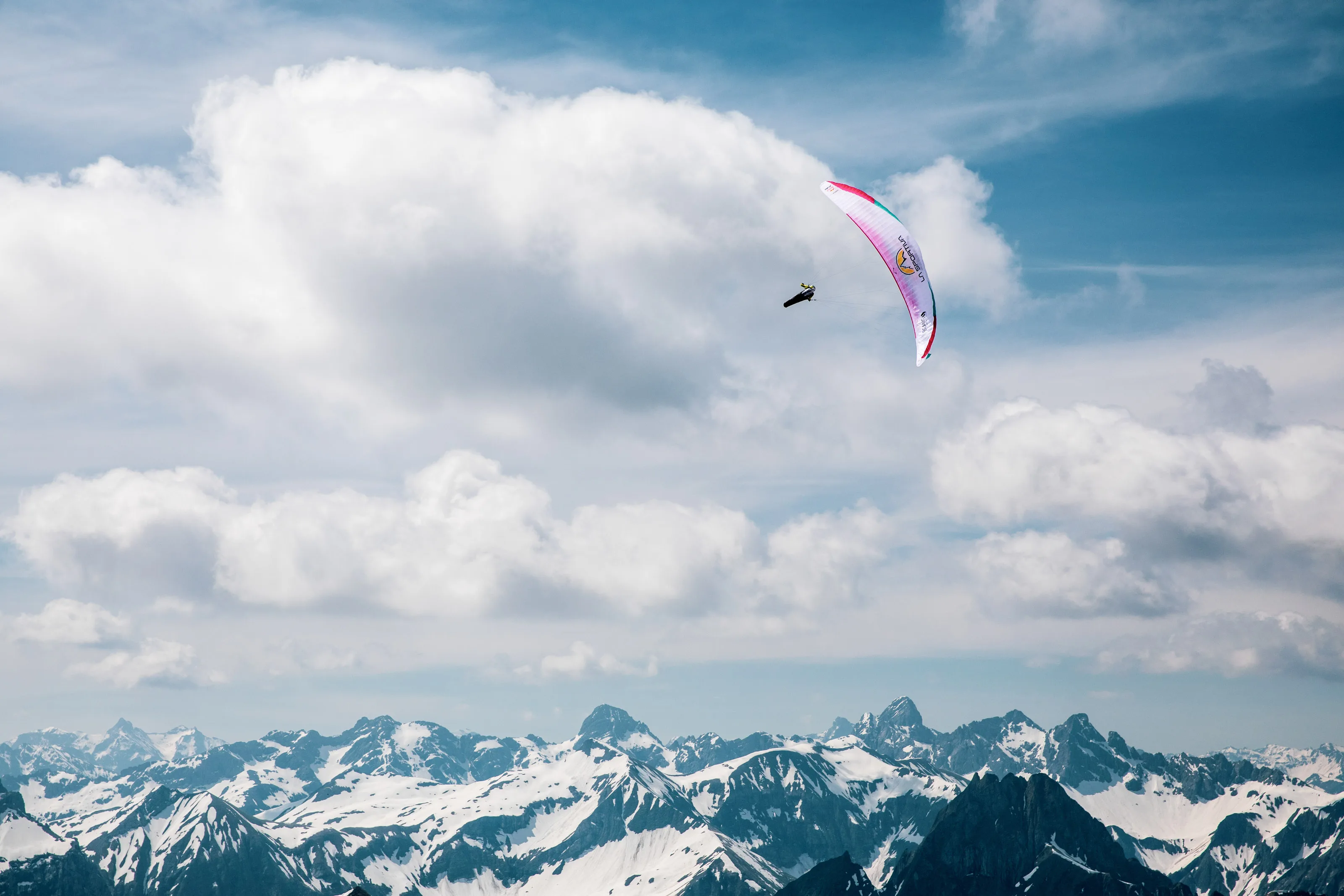 Der Gleitschirm von Michael Lacher fliegt vor mächtigen weißen Wolken und fernen Bergspitzen.