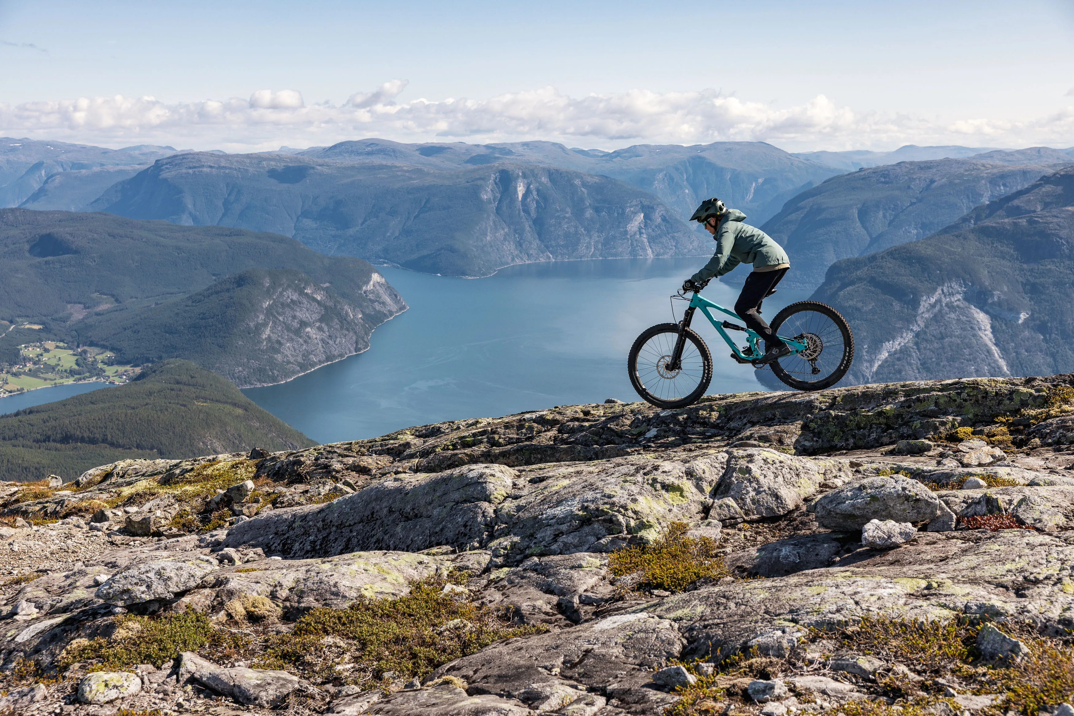 Mountainbiker quert einen felsigen Bergrücken hoch über einem breiten Fjord