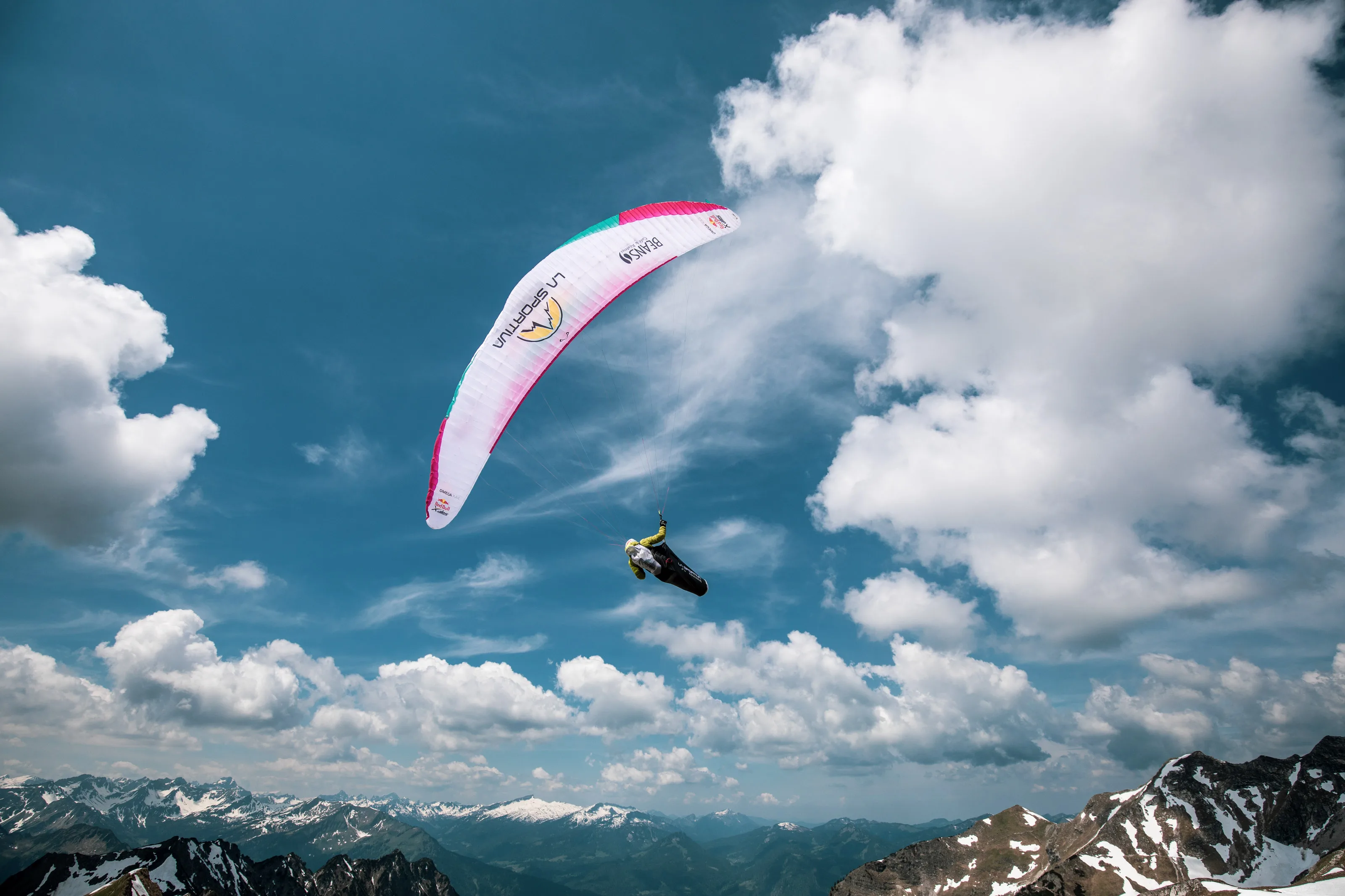 Michael Lacher fliegt in einer Kurve unter seinem pinkweißen Schirm vor hohen Wolken.
