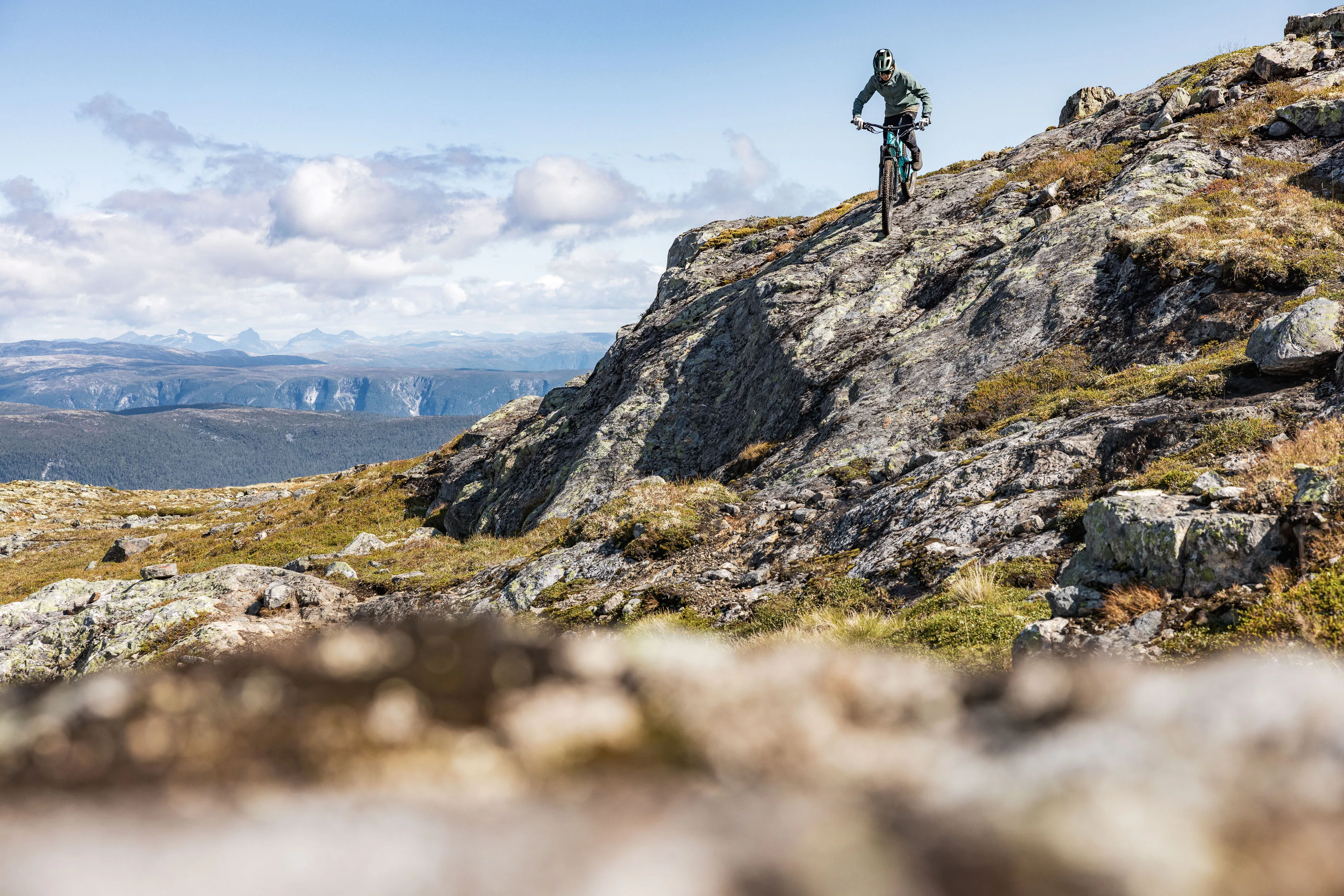 Mountainbiker fährt eine steile Felsstufe auf einem offenen Bergrücken hinab