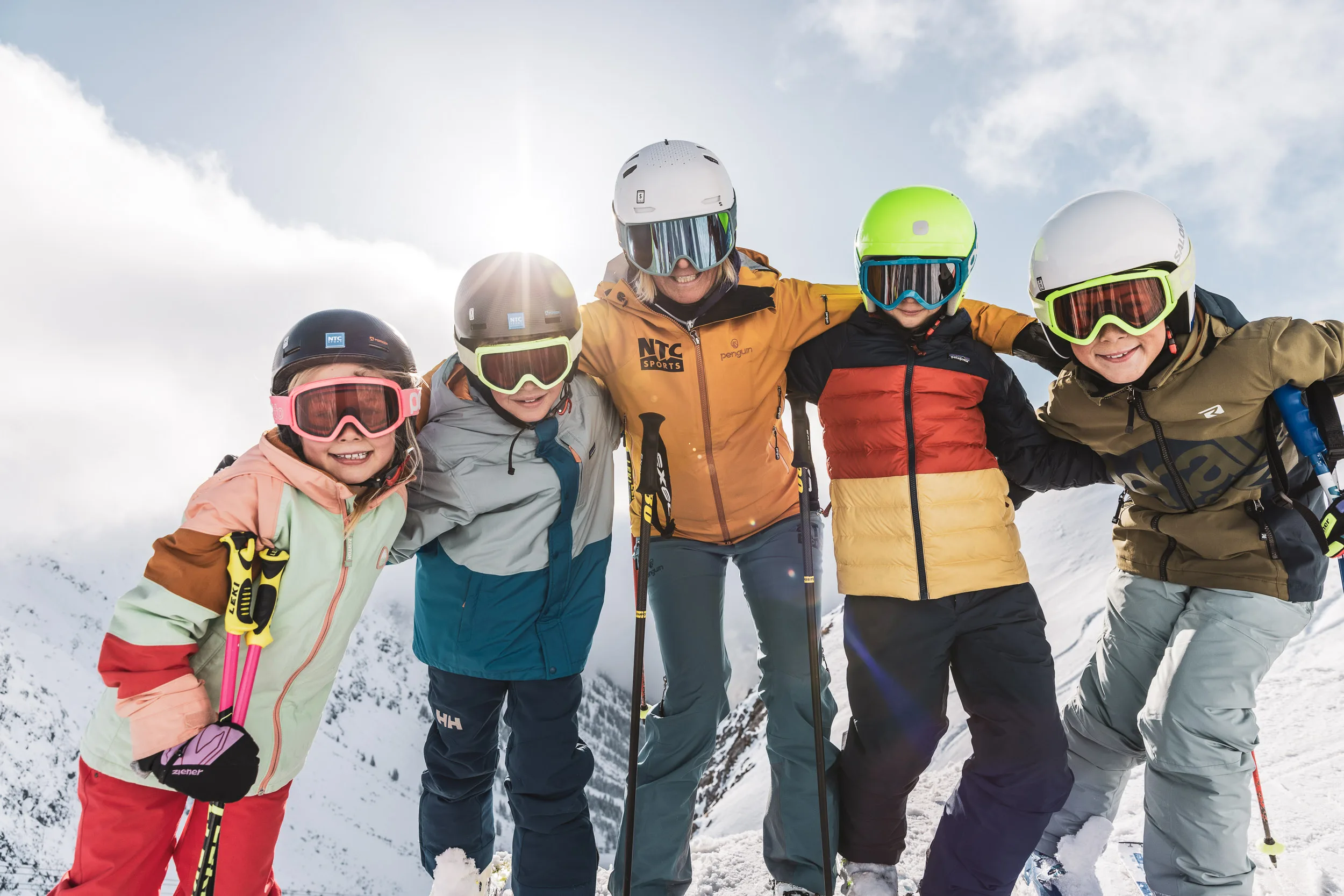 Kinder und Skilehrer stehen gemeinsam vor verschneiten Bergen
