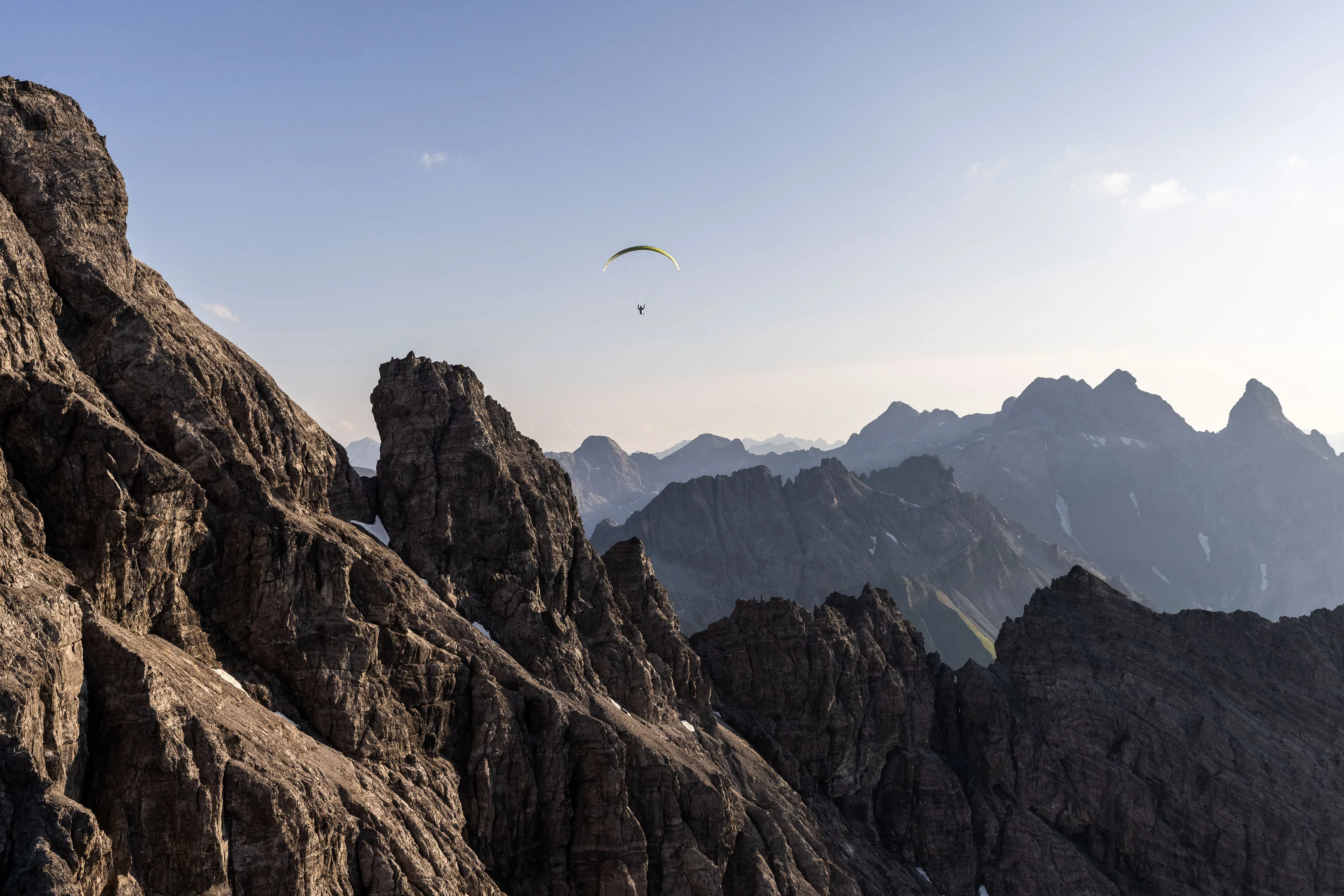 Michael Schnetzer fliegt zwischen dunklen Felstürmen vor einer gestaffelten Bergkulisse