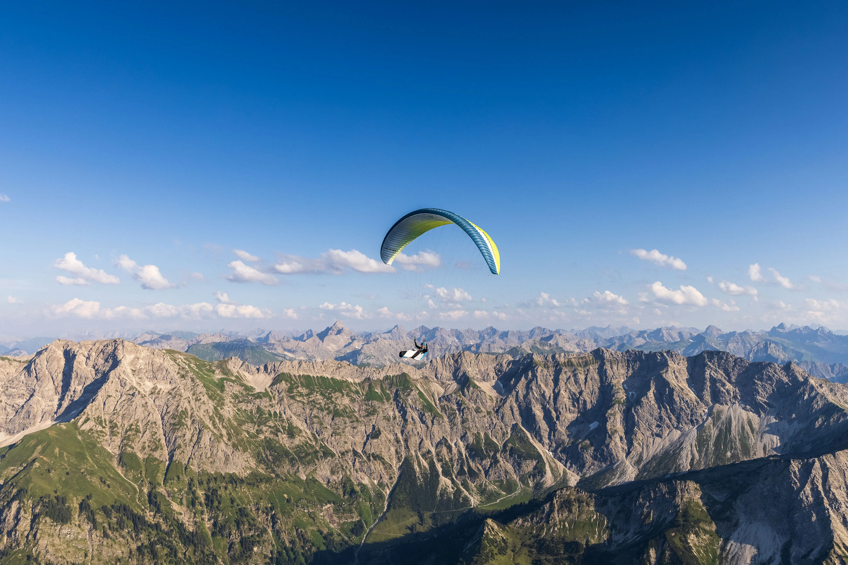 Ein gelber Gleitschirm hebt sich über einer zerklüfteten Berglandschaft ab