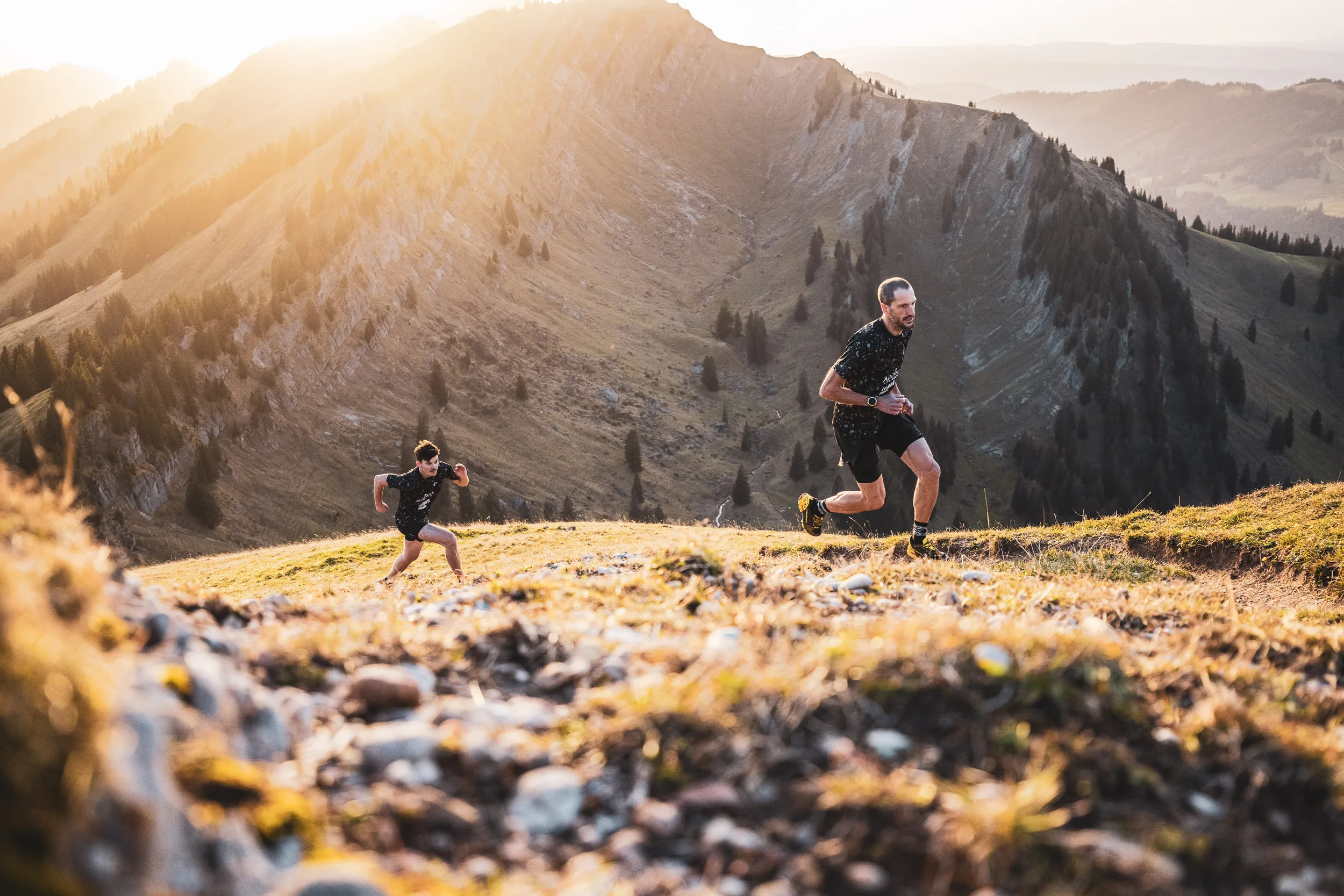 Trailrunner laufen dynamisch am Hang vor der Nagelfluhkette im Abendlicht