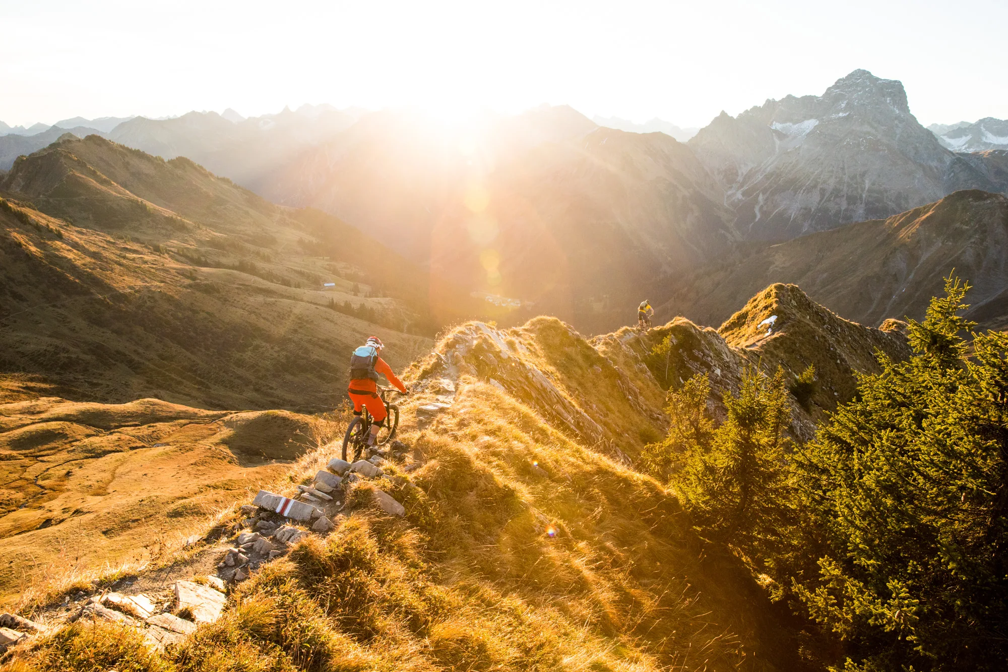Mountainbiker fährt auf einem steinigen Gratweg durch goldenes Licht über dem Kleinwalsertal