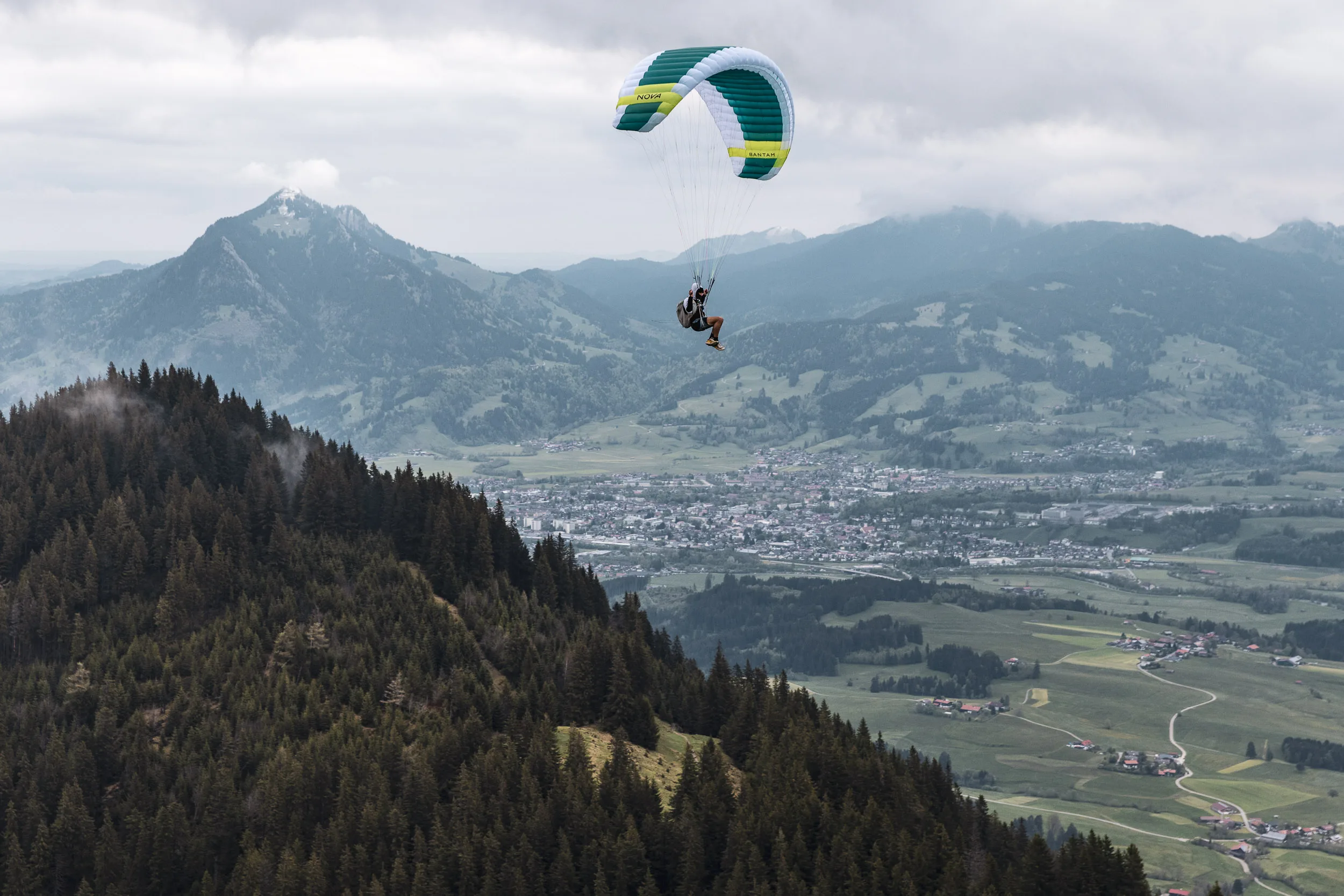 Gleitschirmpilot schwebt über Bergwäldern und Siedlungen im Allgäu