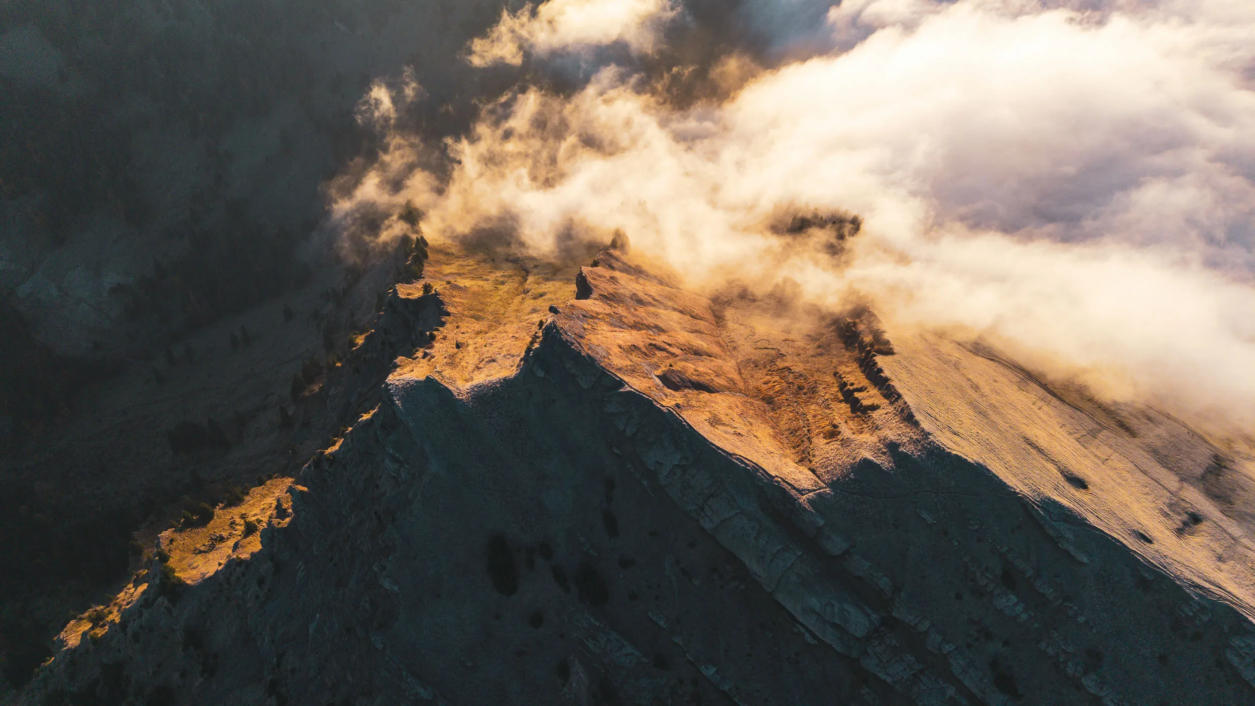 Goldenes Licht zeichnet die Felskante eines von Nebel umströmten Berggrats nach