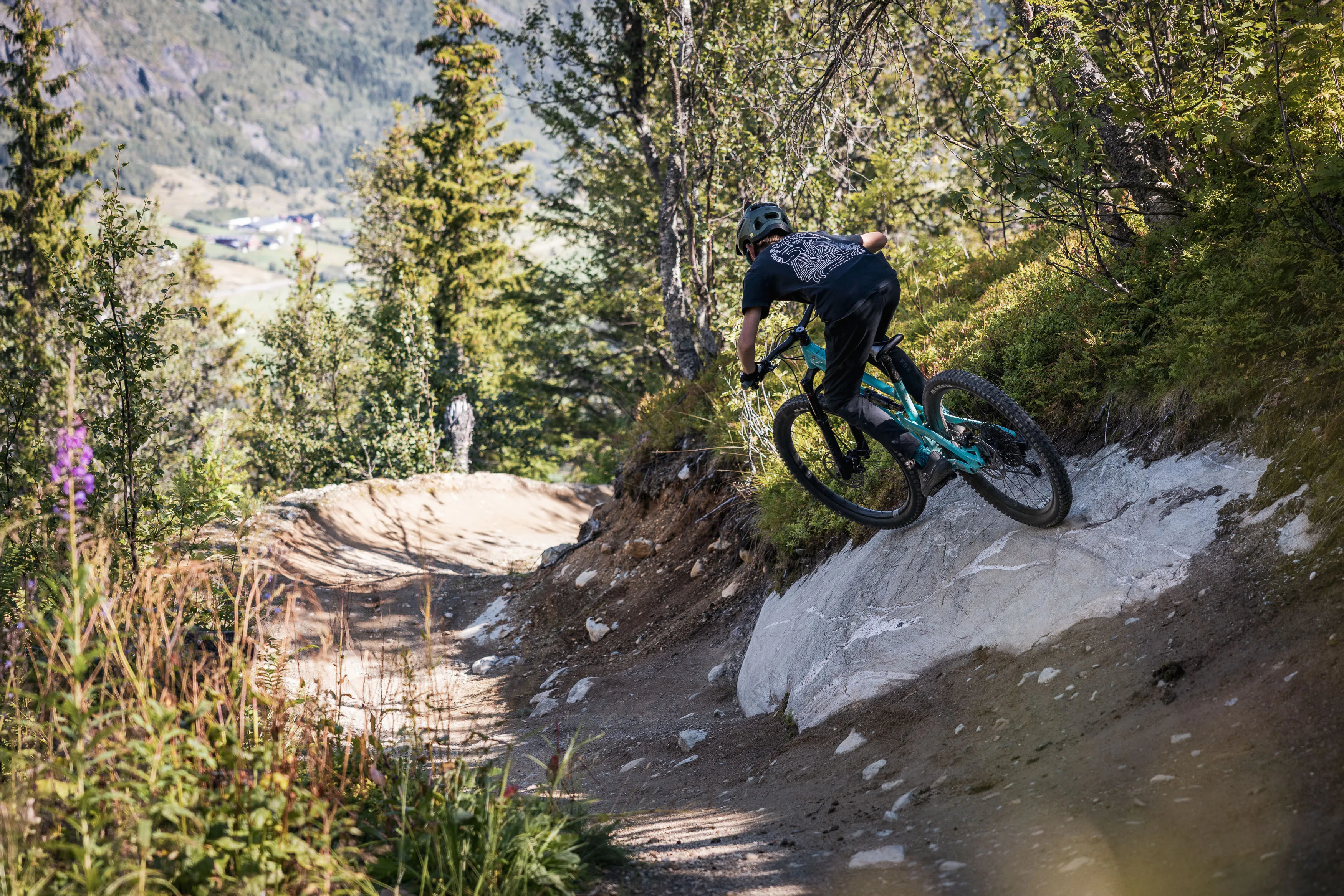 Mountainbiker fährt dynamisch durch eine enge Kurve an einem felsigen Waldhang