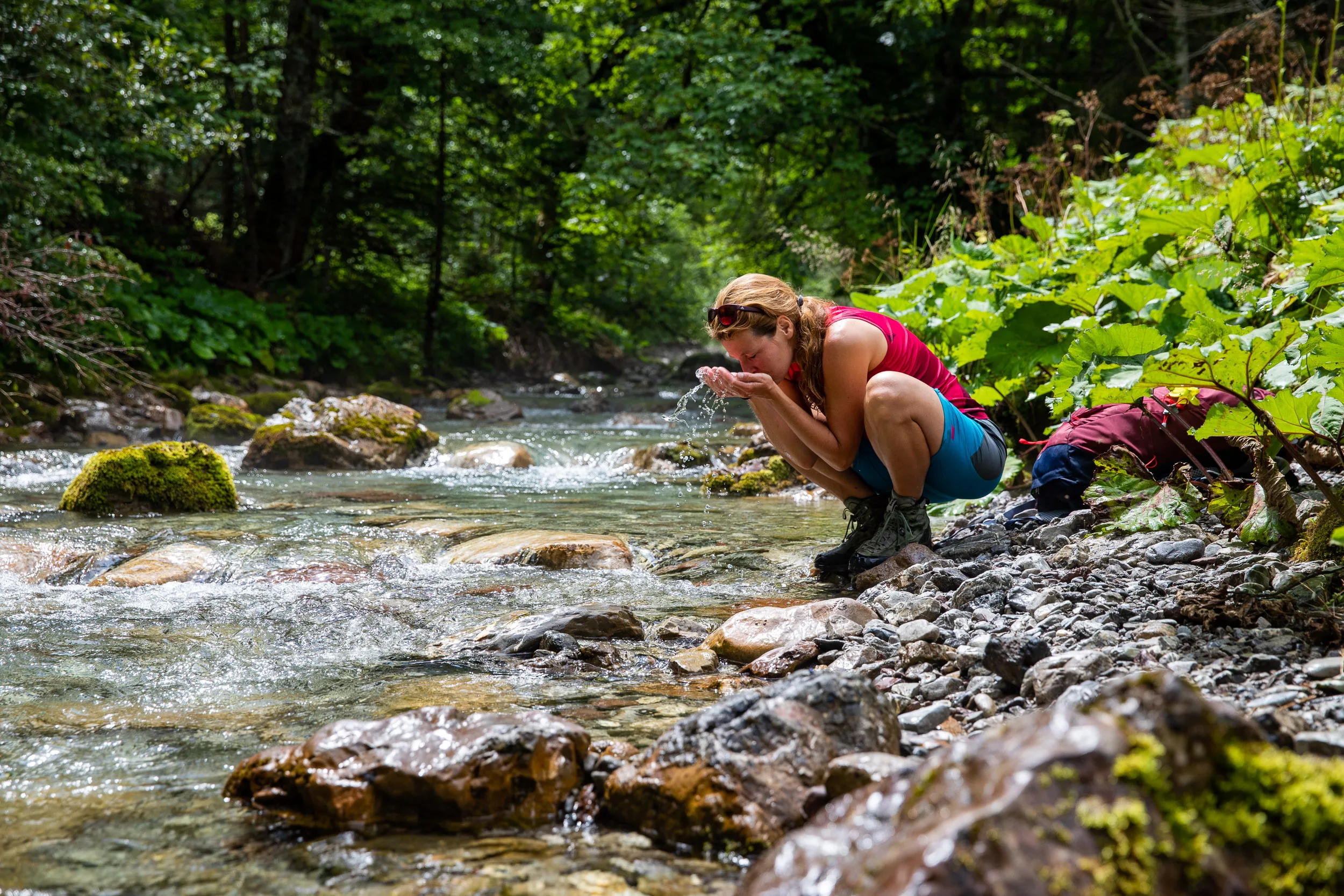 Caroline Nantke kniet an einem klaren Bergbach im schattigen Wald