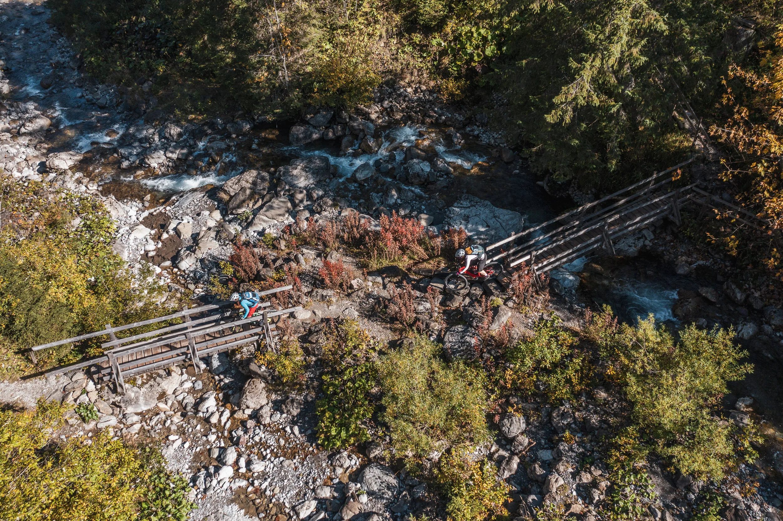 Zwei Mountainbikerinnen überqueren eine Holzbrücke über einem Bach im Kleinwalsertal