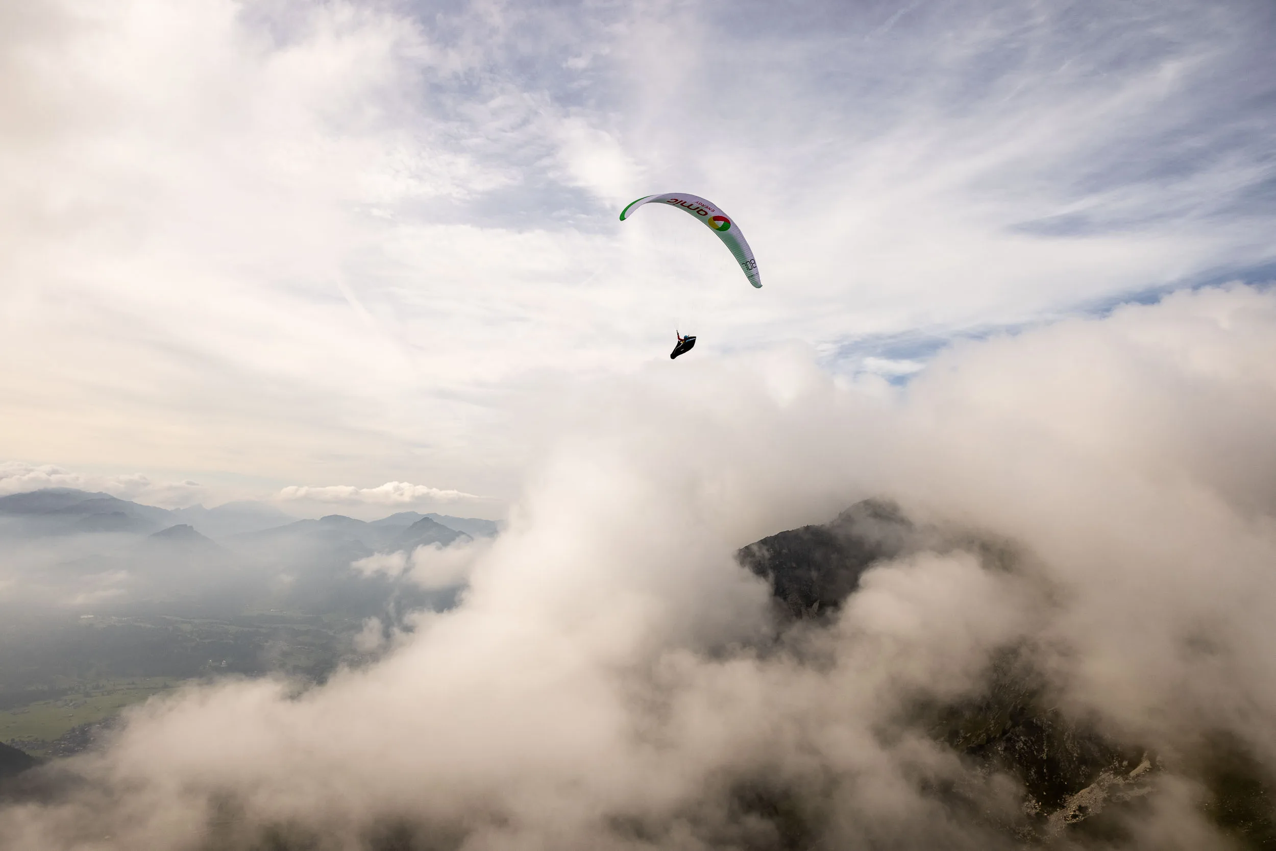 Klaudia Bulgakow fliegt mit ihrem Gleitschirm über Wolken und dem Tal bei Oberstdorf.