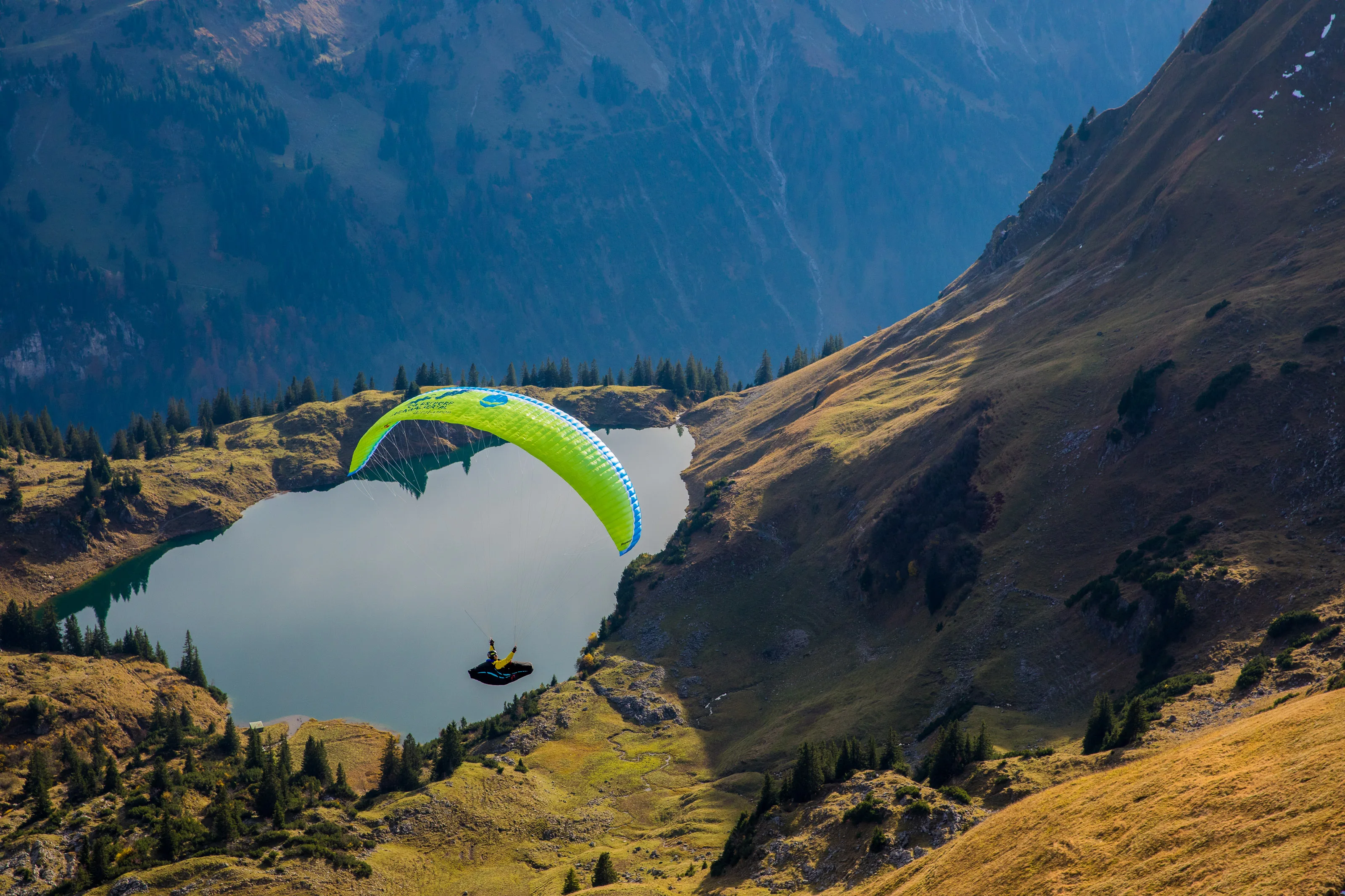 Michael Gebert mit grünem Gleitschirm über dem klaren Seealpsee zwischen herbstlichen Hängen im Allgäu