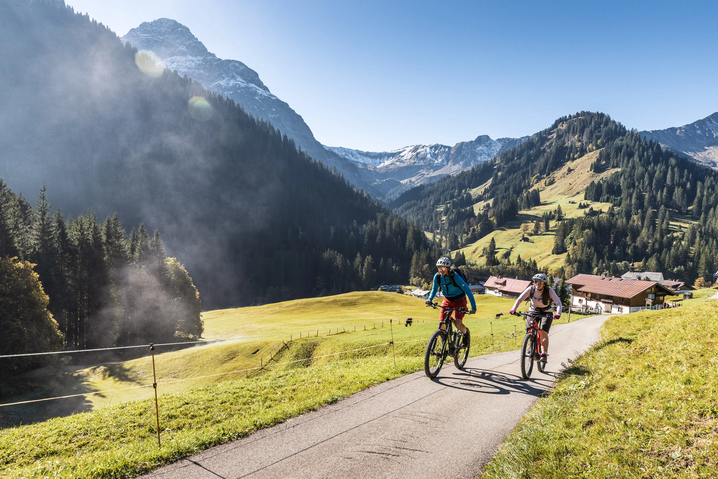 Silvi Vogel und Andrea Geiger fahren im Morgenlicht über eine Bergstraße im Kleinwalsertal