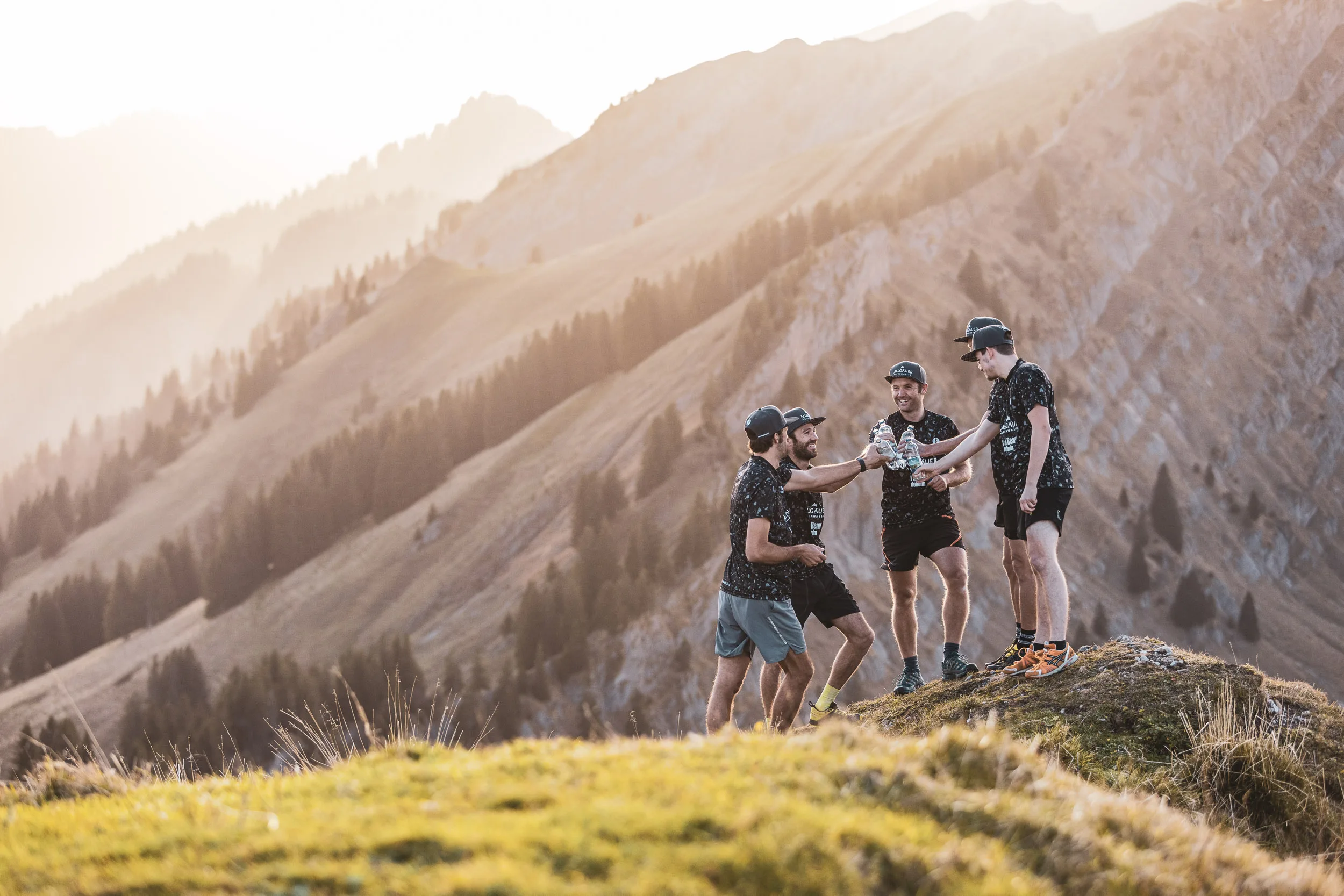 Trailrunning-Team steht auf einem Grat vor steilen Grasbergen