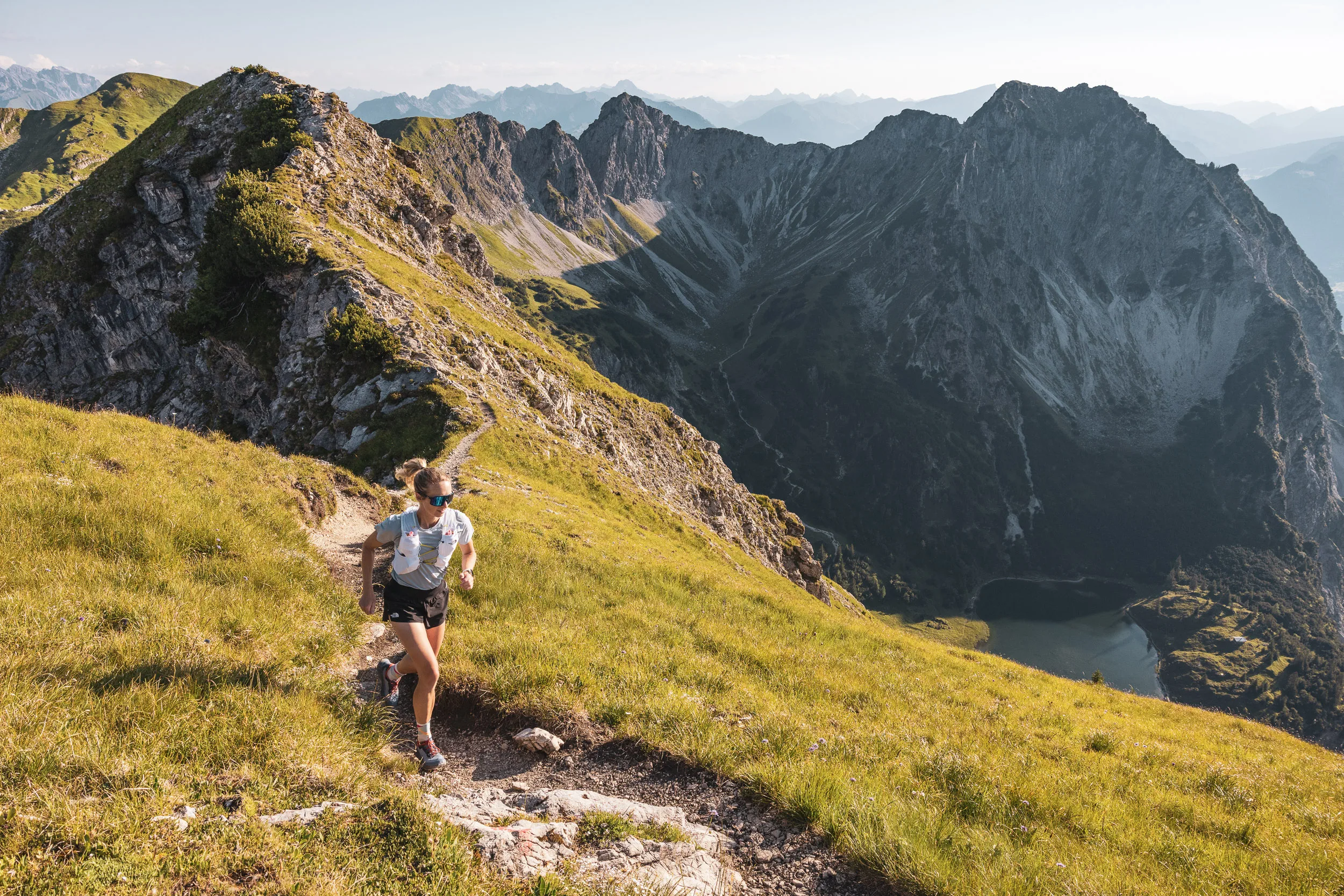 Ronja Morell läuft oberhalb eines Bergsees über einen sonnigen Grashang