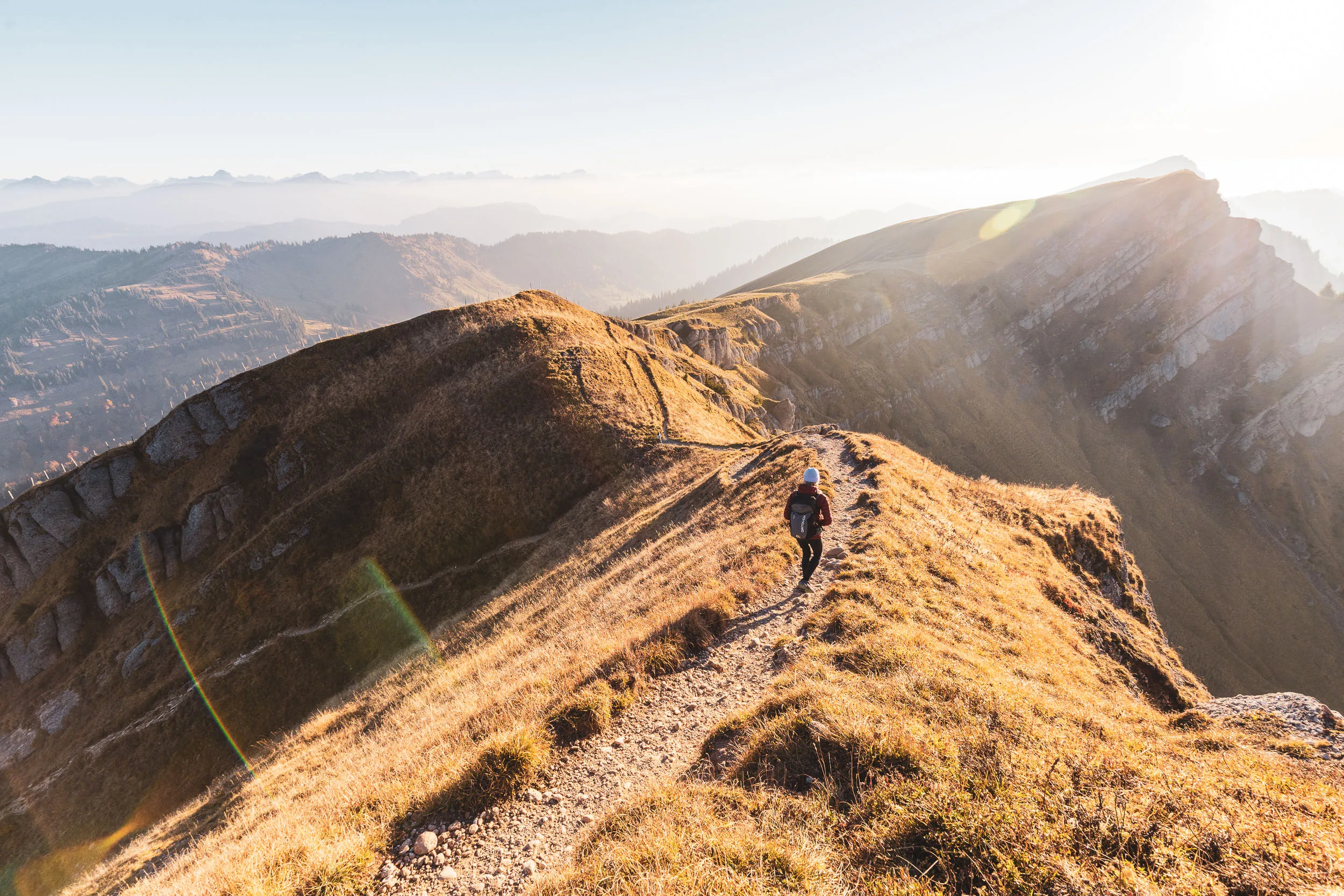Wanderin geht über einen schmalen Gratweg durch warmes Streiflicht