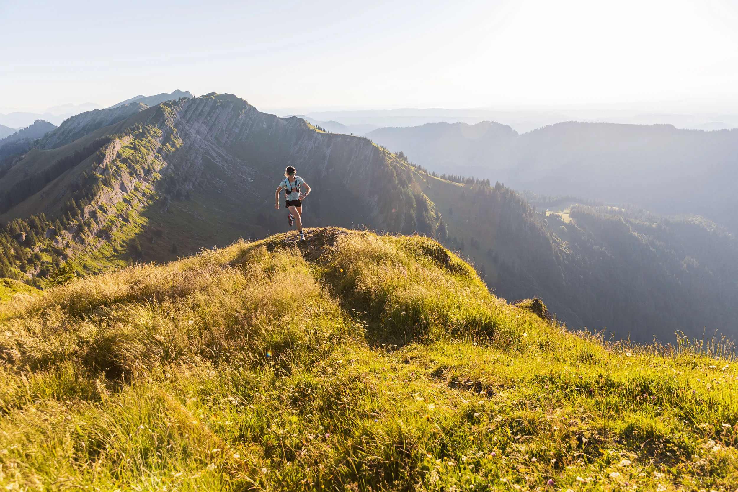 Eine Trailrunnerin läuft über eine grasige Bergkuppe vor den schroffen Flanken der Nagelfluhkette.