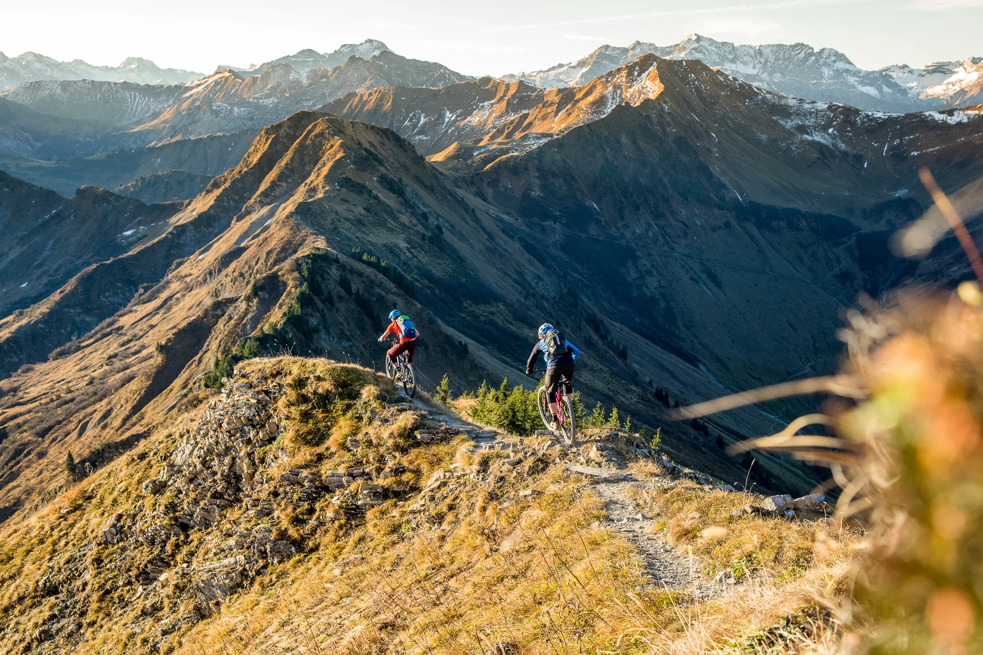 Zwei Mountainbiker rollen auf einem offenen Kammweg durch die herbstliche Berglandschaft