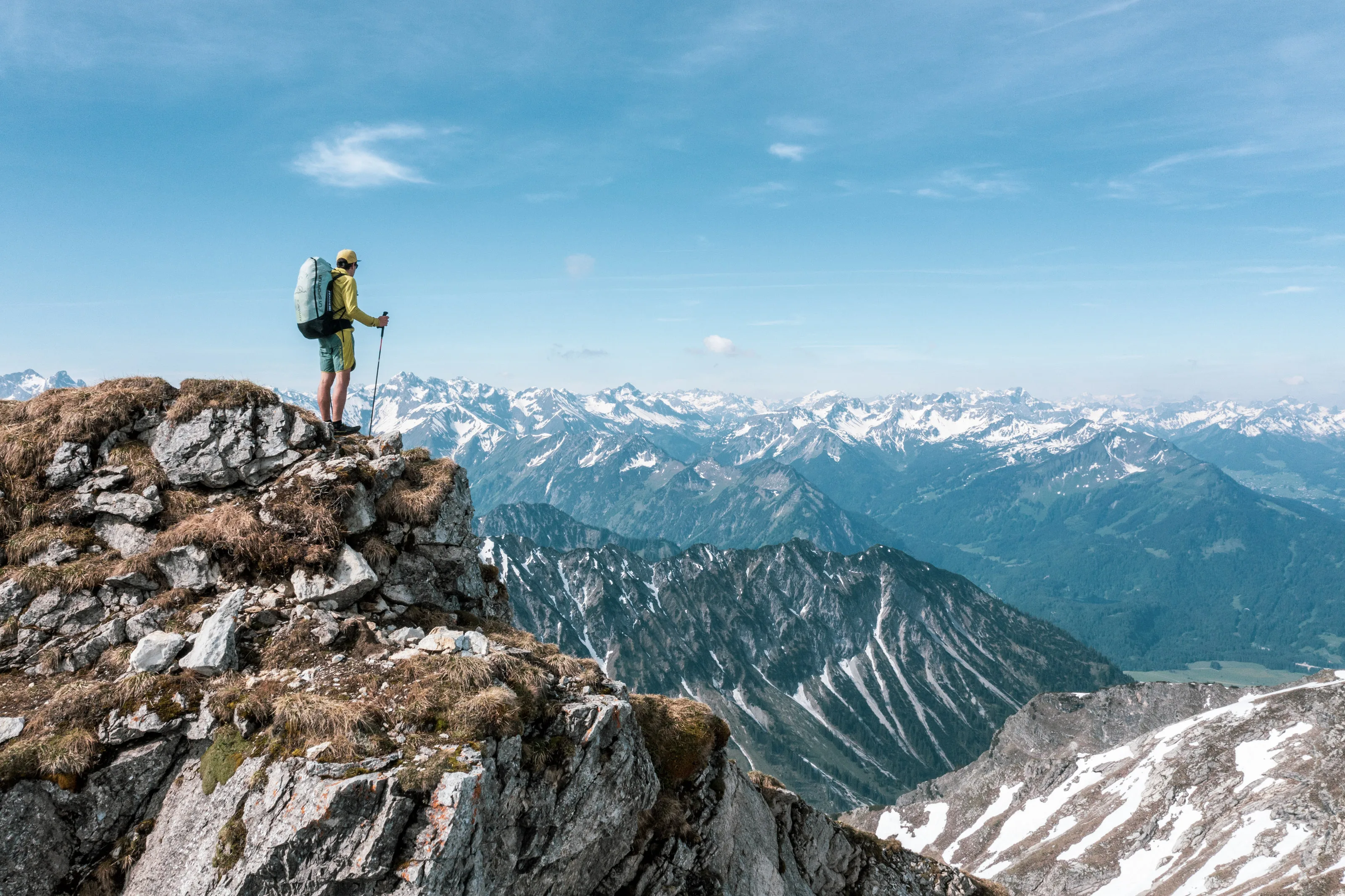 Michael Lacher steht mit Stöcken und Gleitschirmausrüstung auf einem schmalen Grat vor den Allgäuer Alpen.