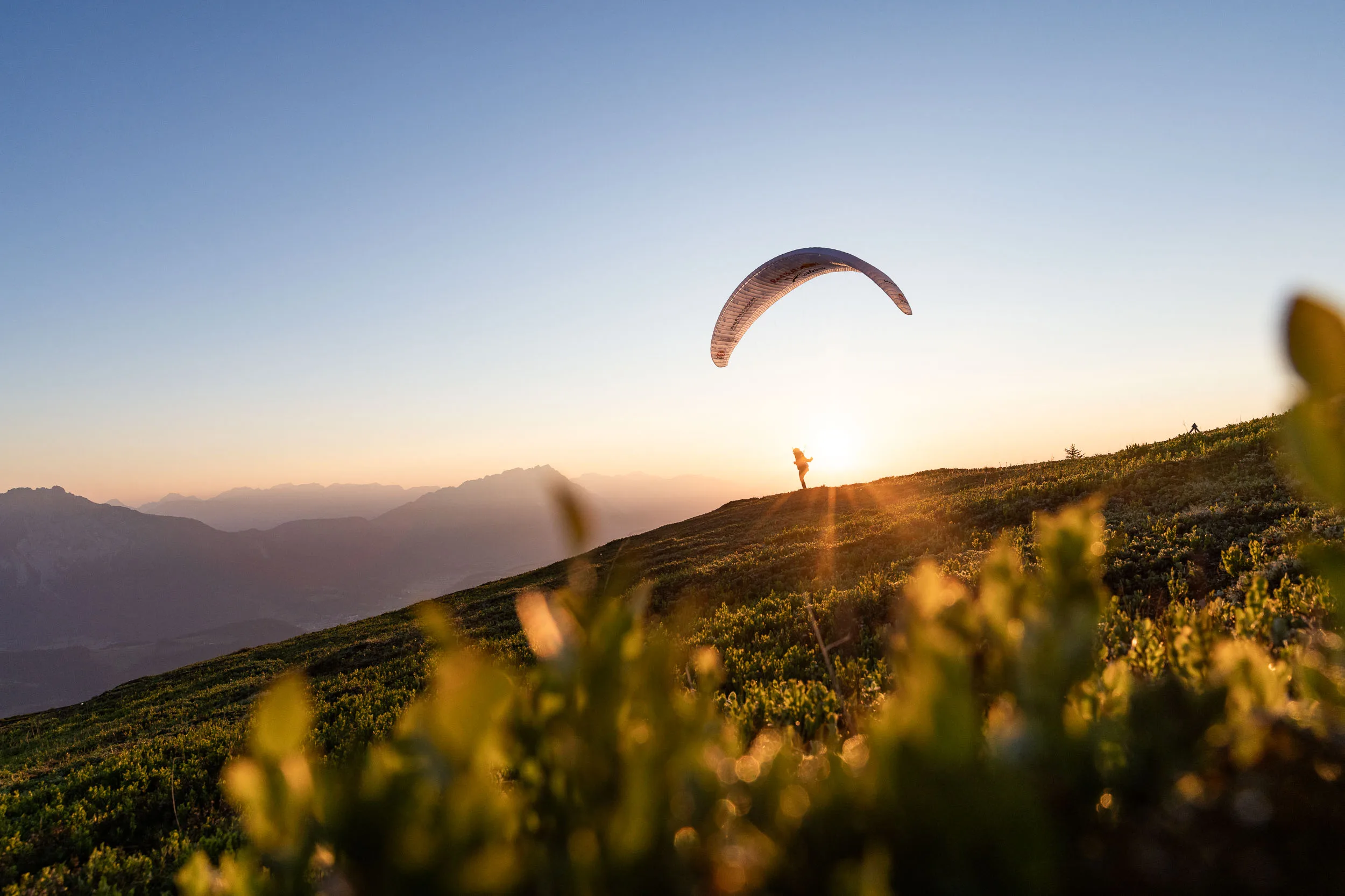 Gleitschirm ueber einer alpinen Wiese im Ennstal bei Sonnenaufgang
